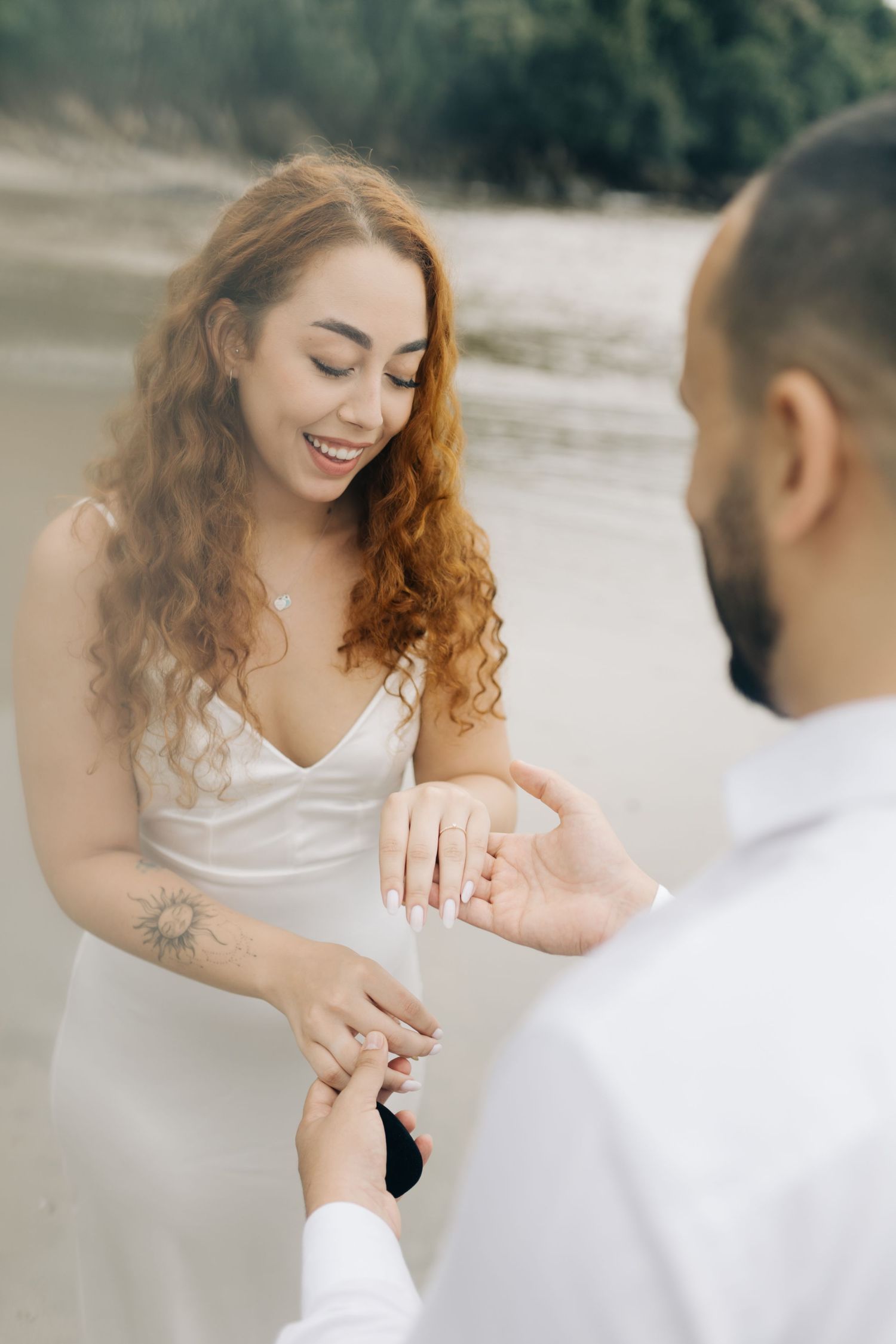 Couple sharing a tender moment examining ring during beach proposal.