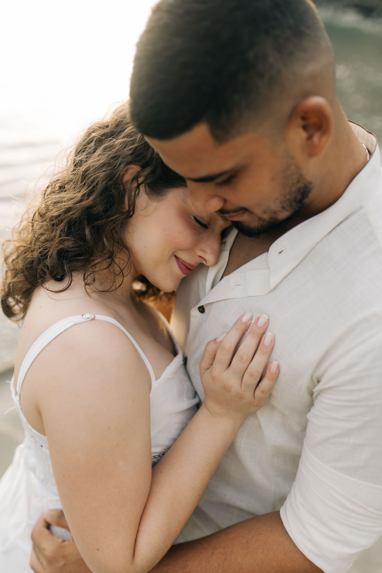 Couple in white embracing tenderly on a beach during sunset.