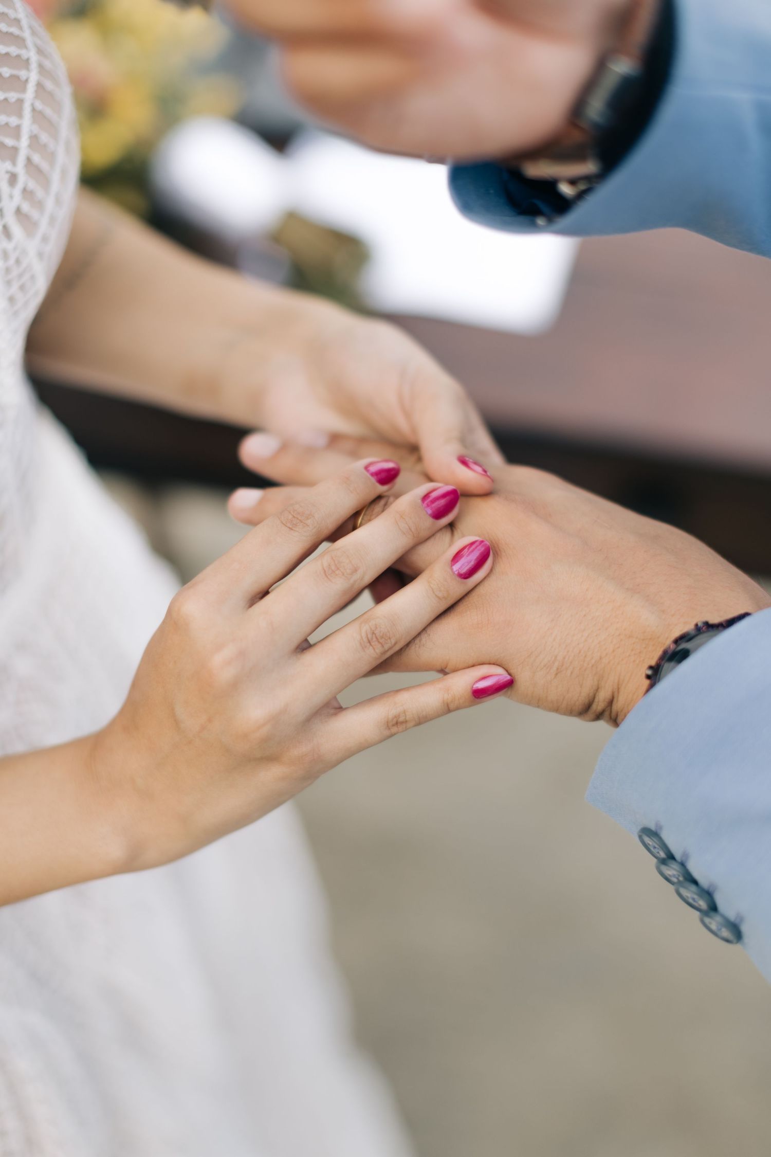 Close-up of hands during ring exchange ceremony showing pink manicured nails.
