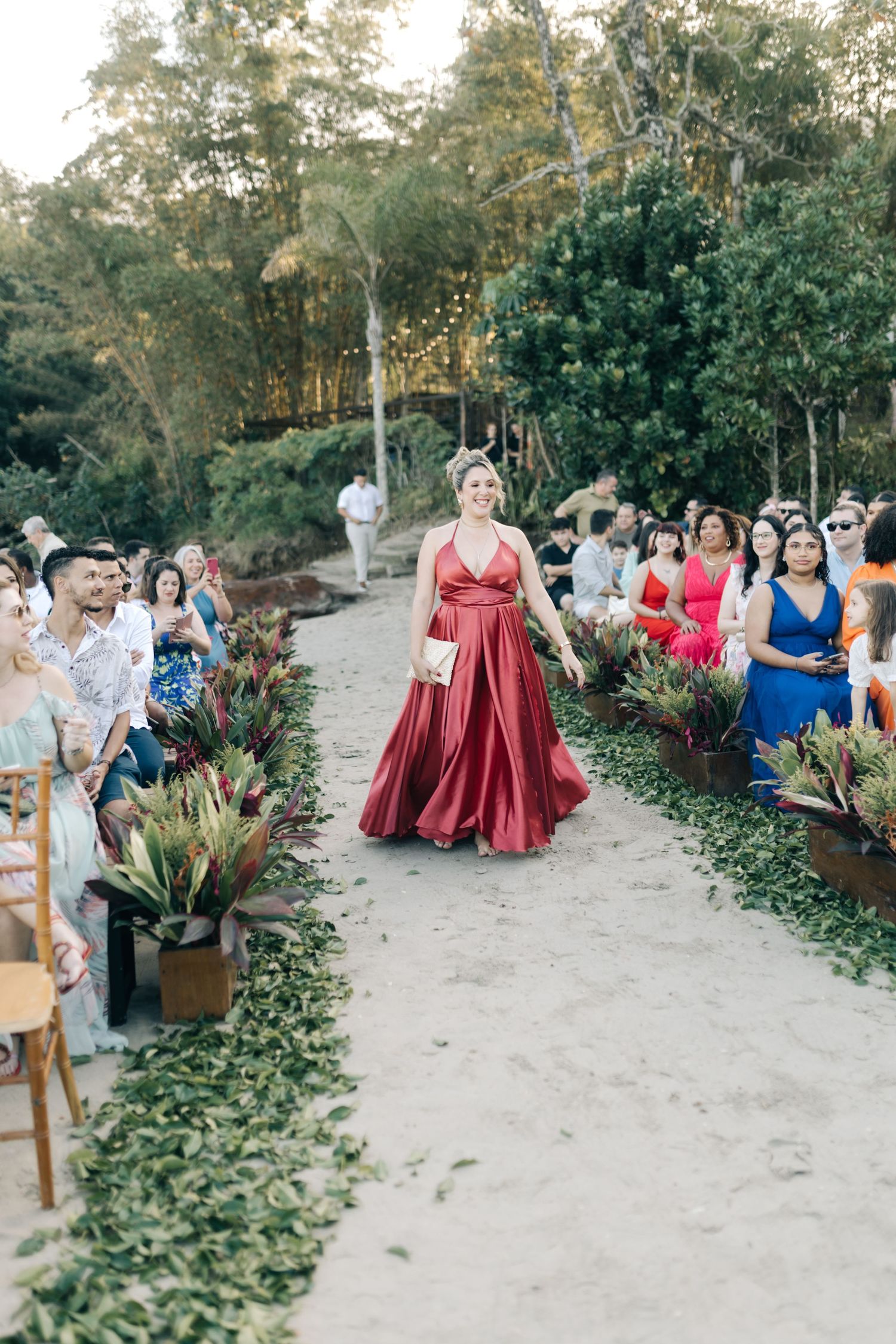 Wedding guests in colorful attire seated on chairs during an outdoor beach ceremony.
