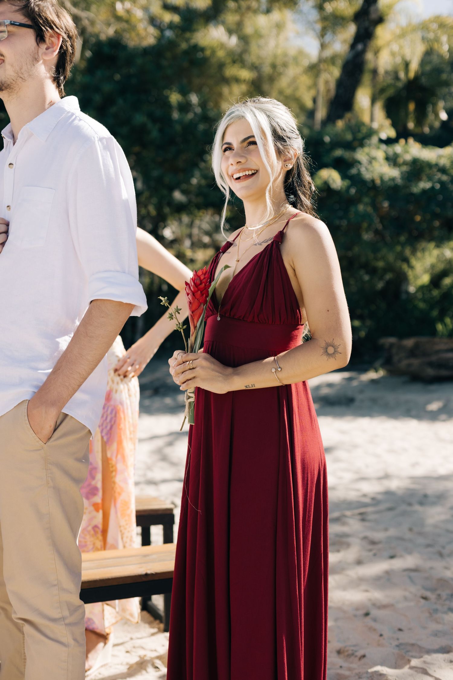 Wedding guest in burgundy dress holding flowers at outdoor celebration.