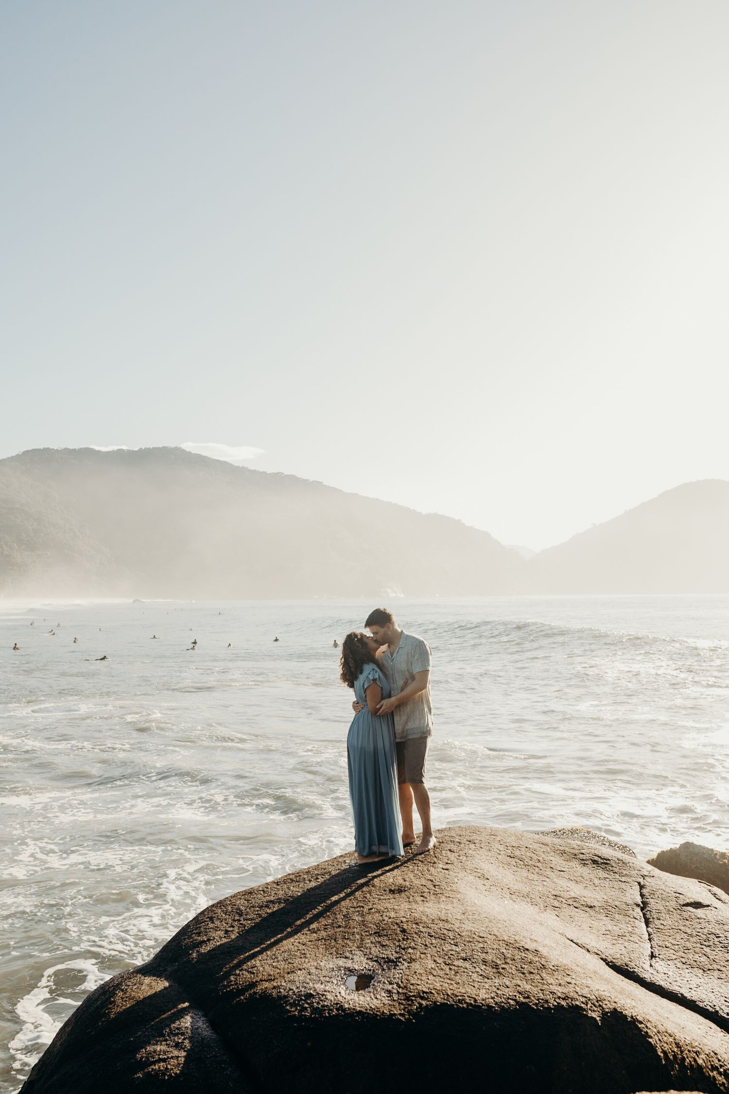 Silhouetted couple embracing on rocky overlook with foggy coastal landscape behind them.