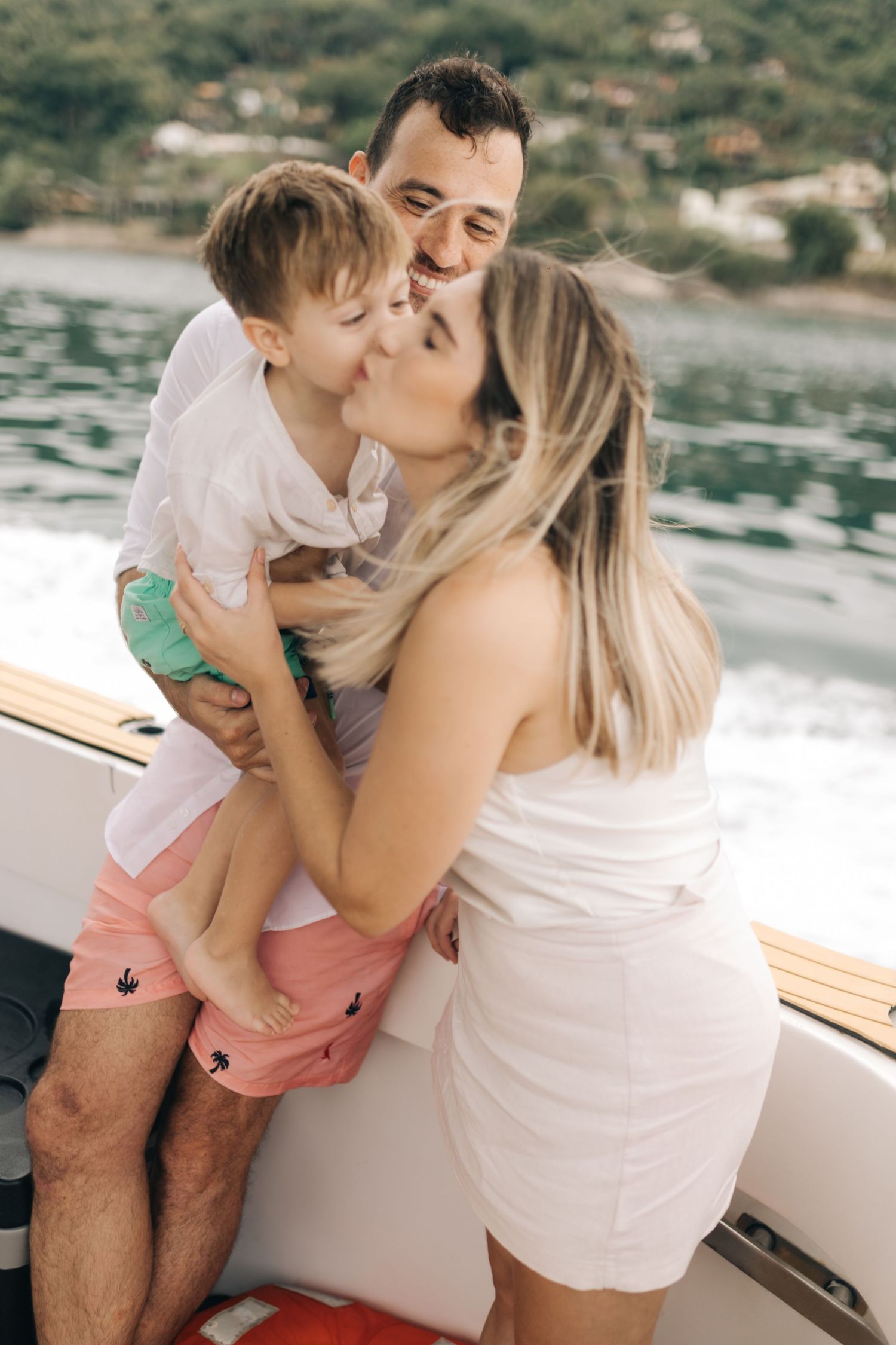 Family sharing tender moment together on boat with ocean and hills in background.