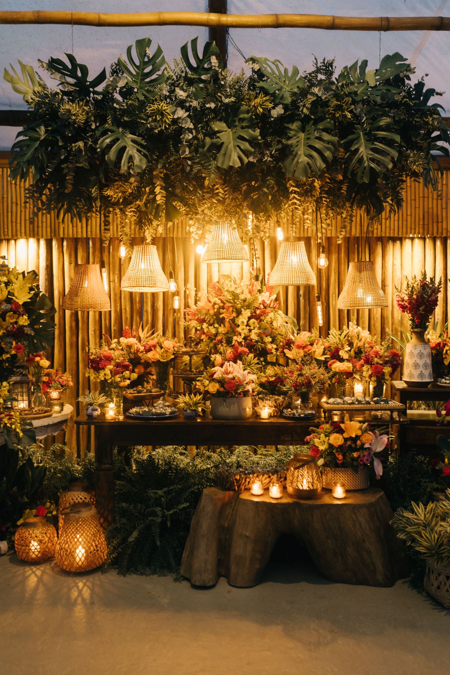 Wedding reception decor featuring rustic burlap, glowing lanterns, and cascading floral arrangements on dark tables.