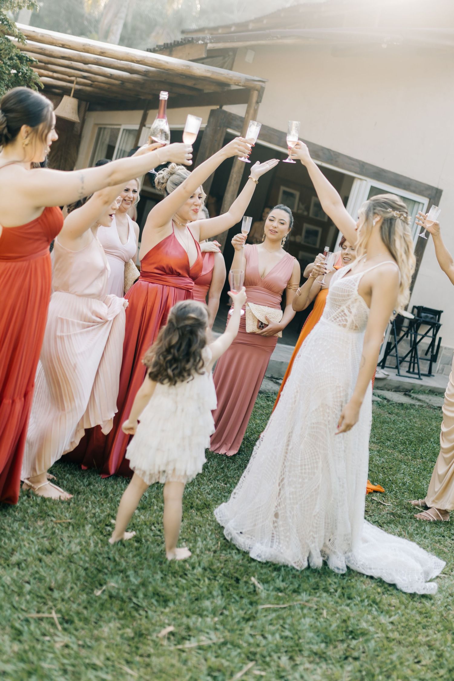 Wedding party raises glasses in a toast on a lawn with the group wearing pink and coral dresses.
