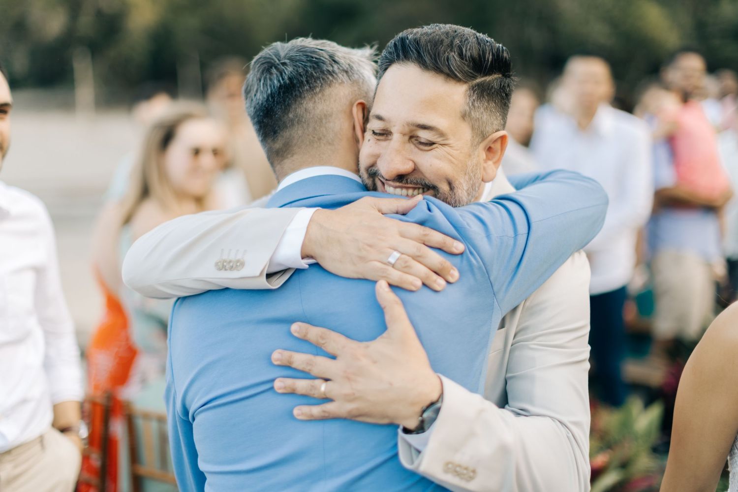 Heartfelt embrace between two wedding attendees in light blue and white suits.