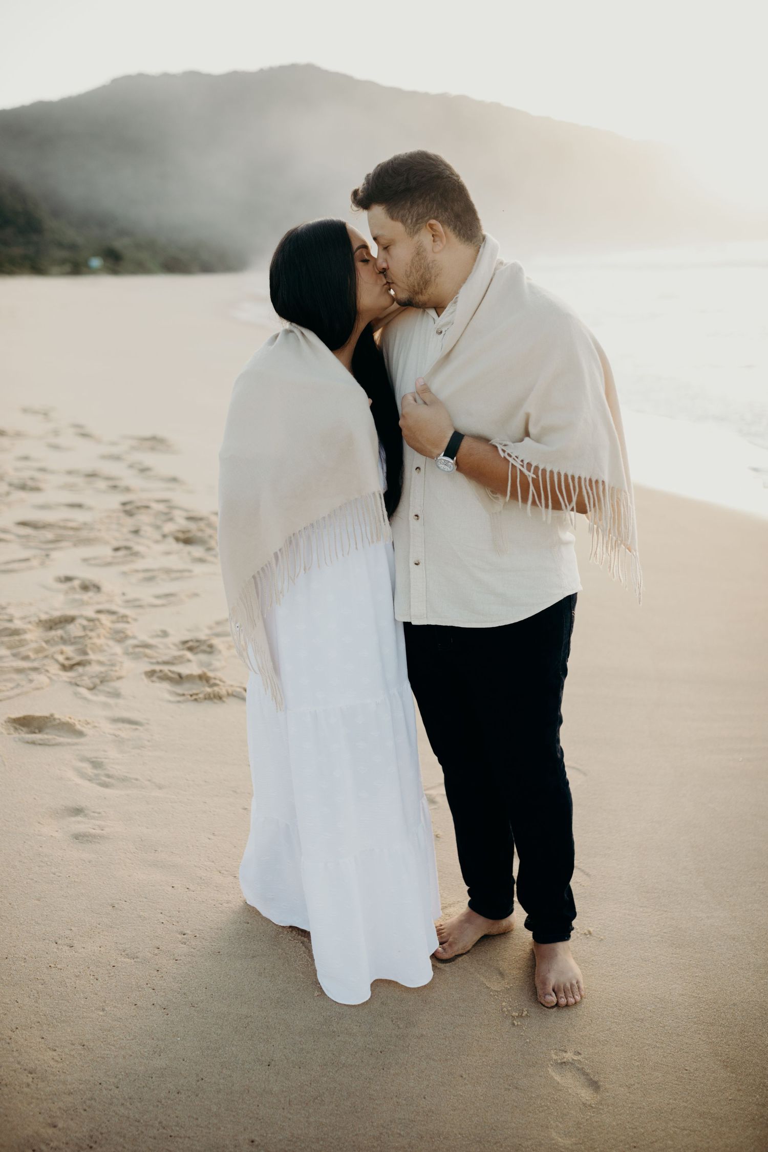 Romantic beach photoshoot with couple embracing on the sand at golden hour.
