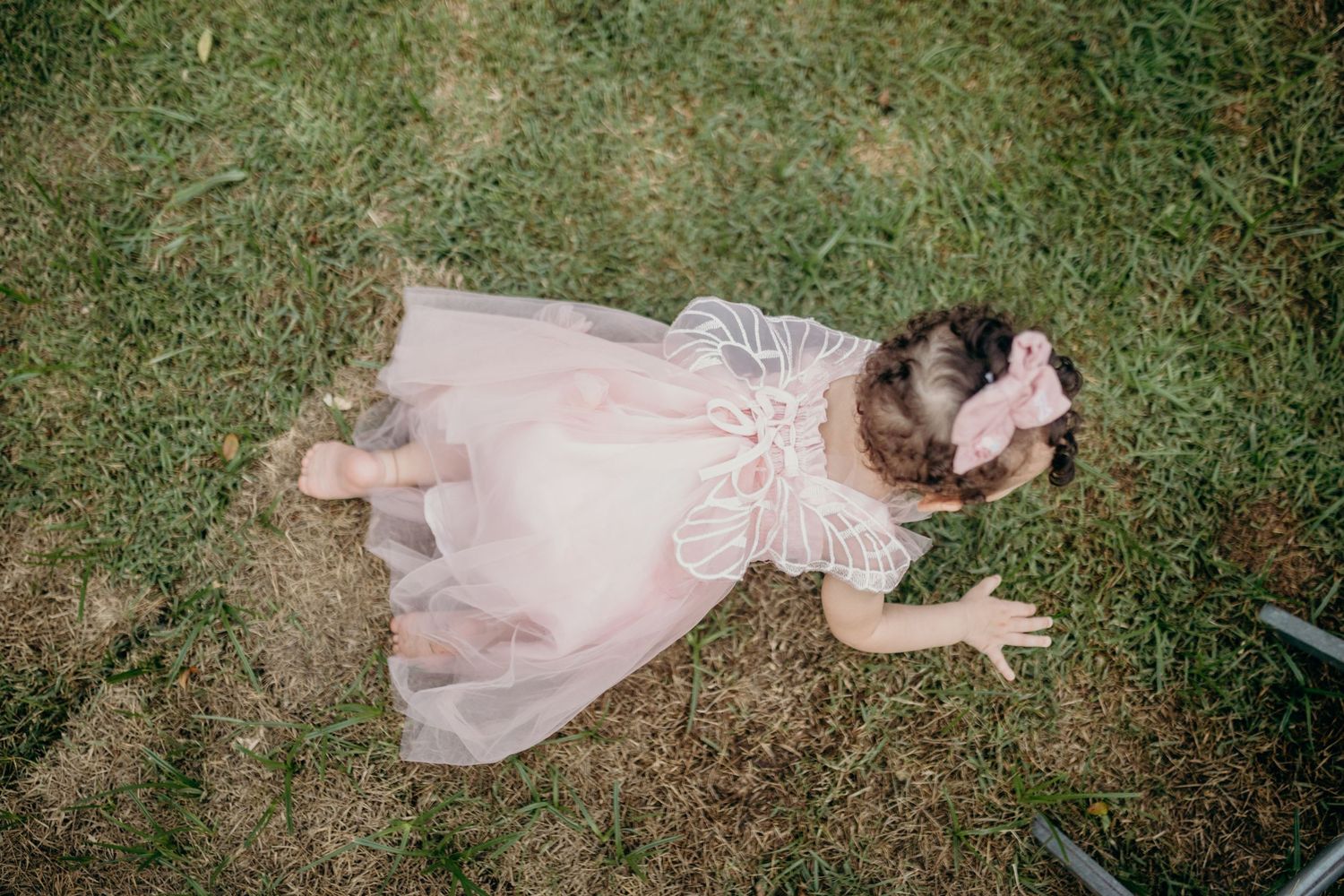 Child in pink dress lying on grass during outdoor photoshoot.