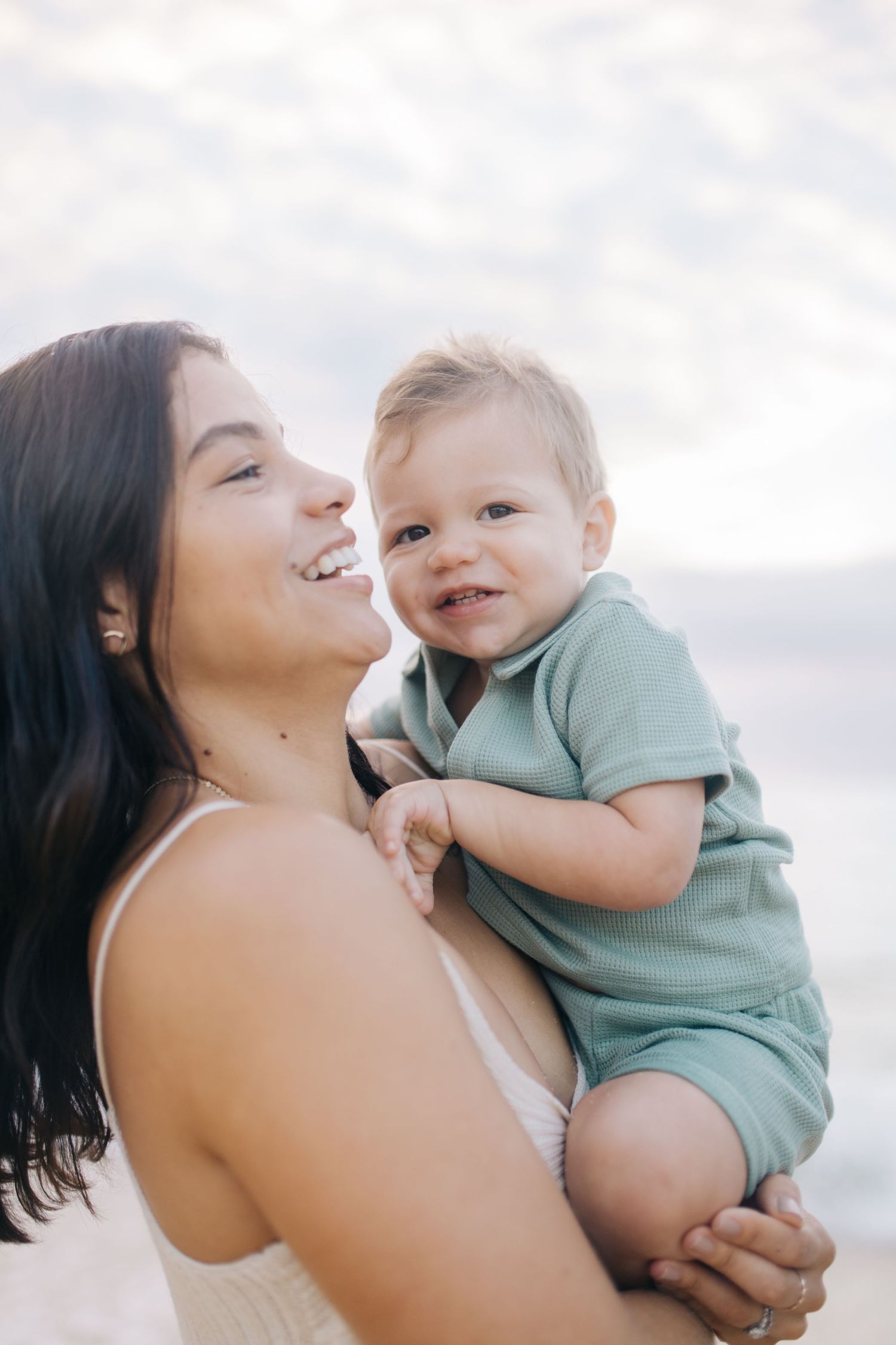 Mother and baby share tender moments of affection at a bright beach setting.