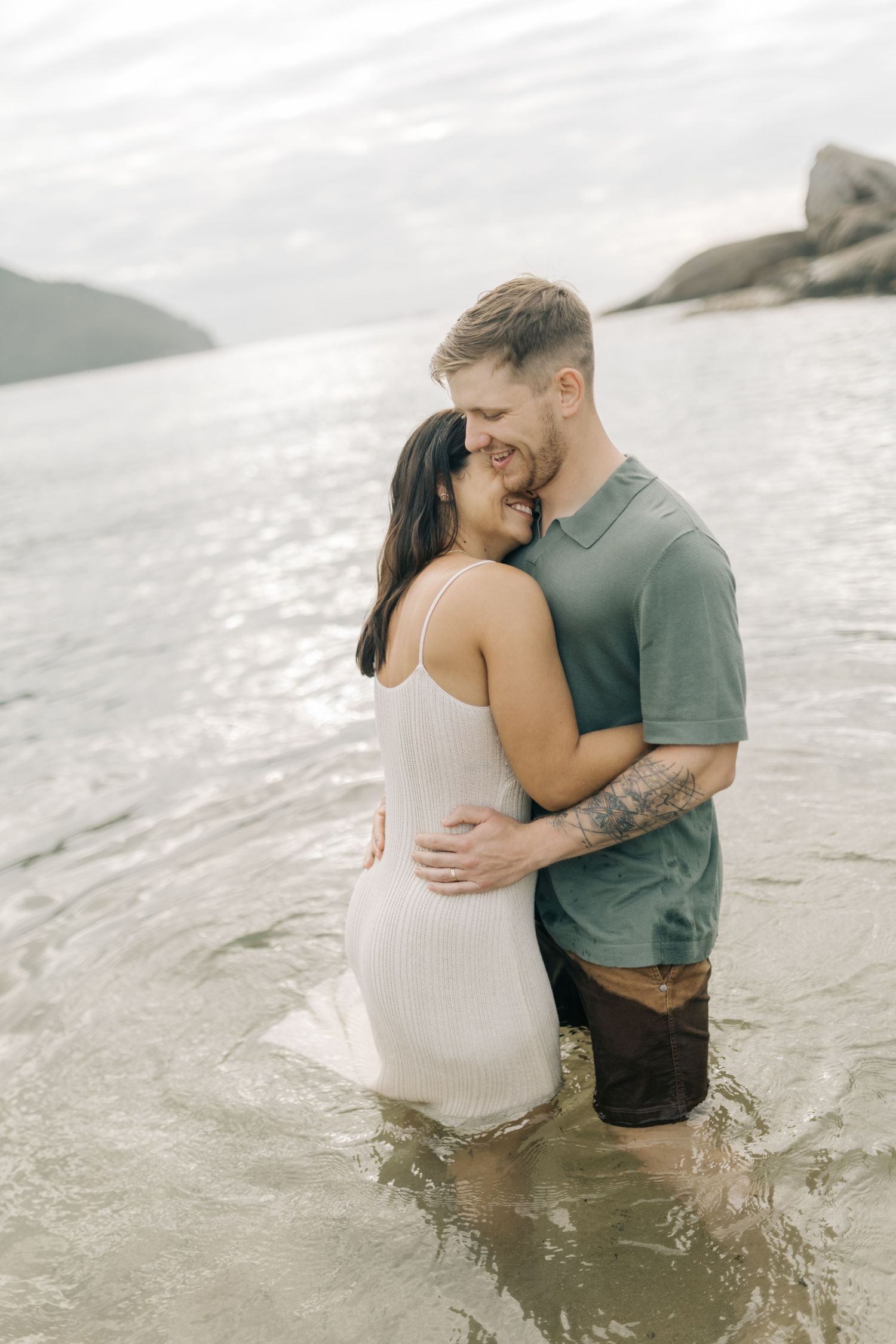 Couple wading in shallow ocean water at a scenic beach during sunset.