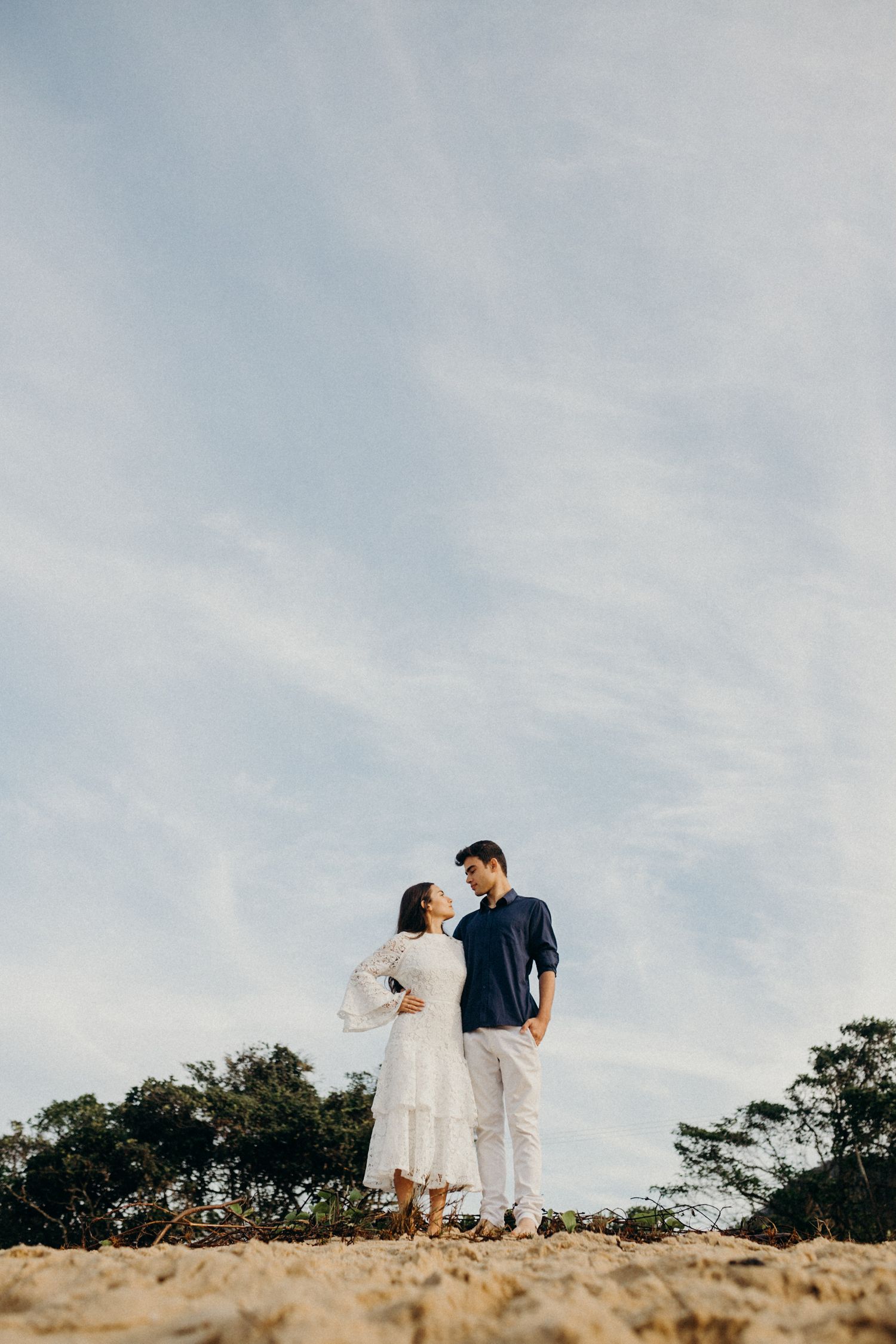 A romantic couple poses together on a hilltop against a cloudy sky background.