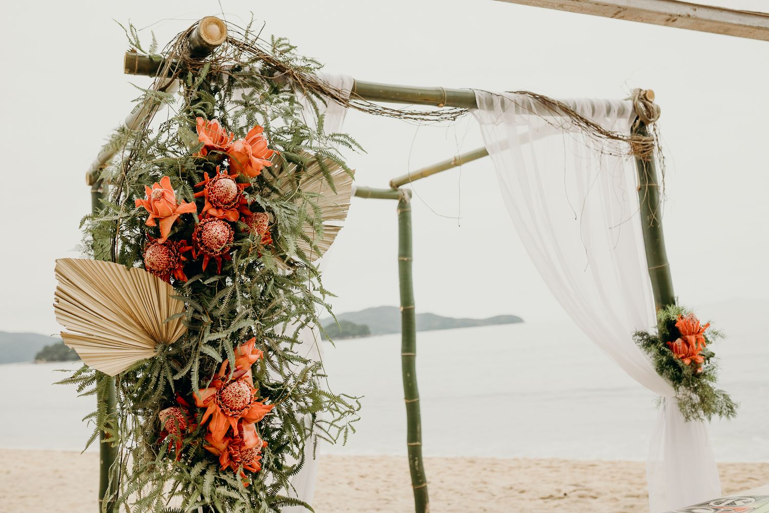 Beach wedding ceremony setup with floral arch and natural decor against ocean backdrop.