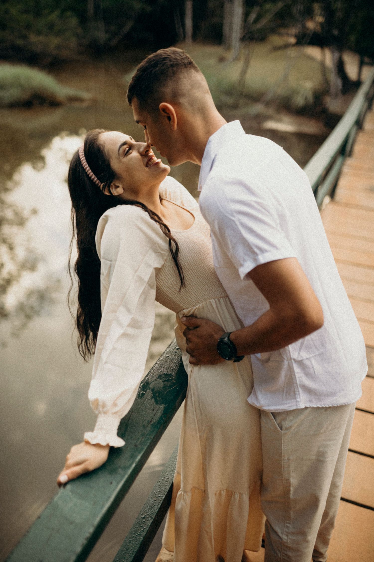 Couple in white clothing sharing playful moments on a wooden bridge.