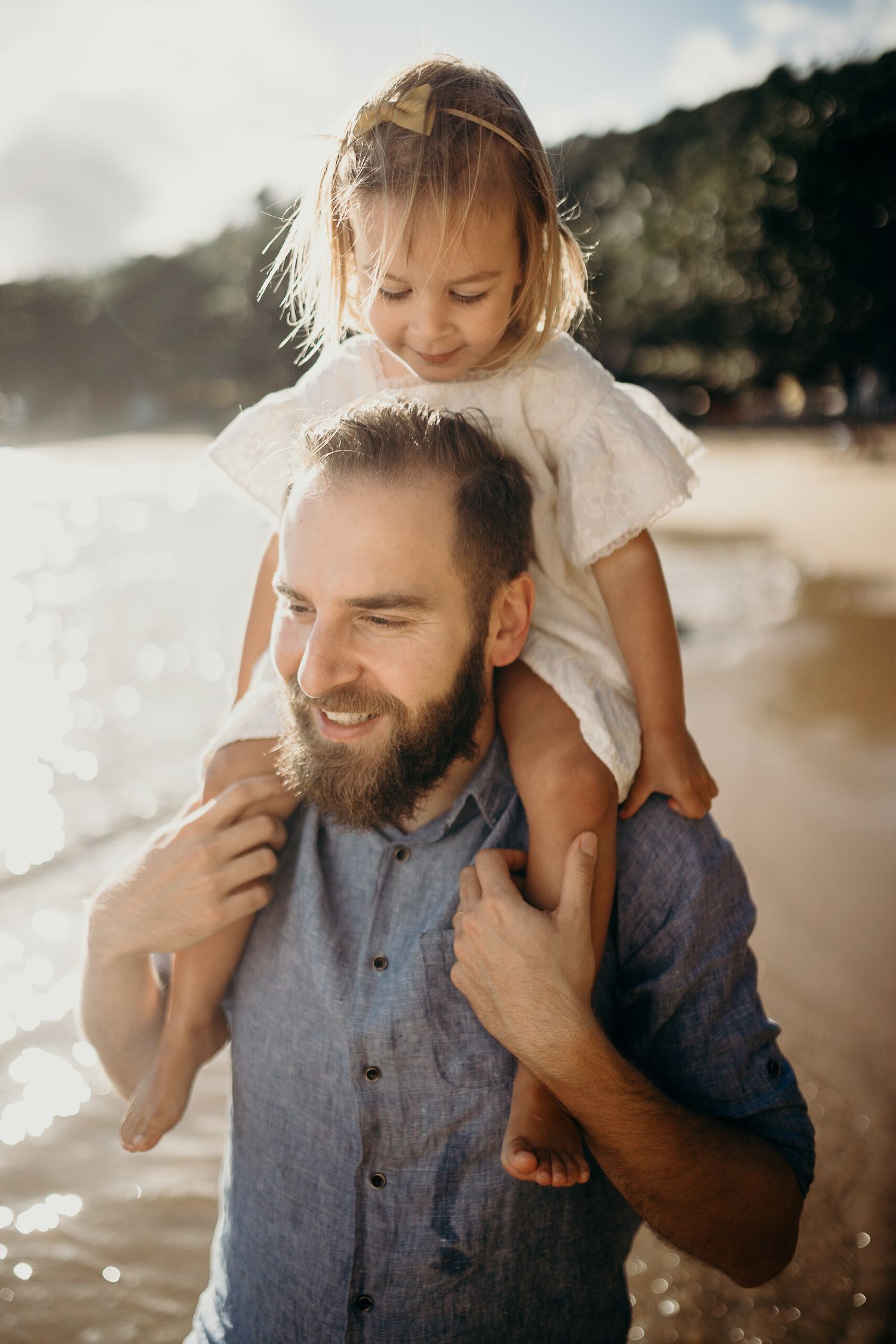 A playful beach moment between a parent and child with sunlit ocean waves in the background.