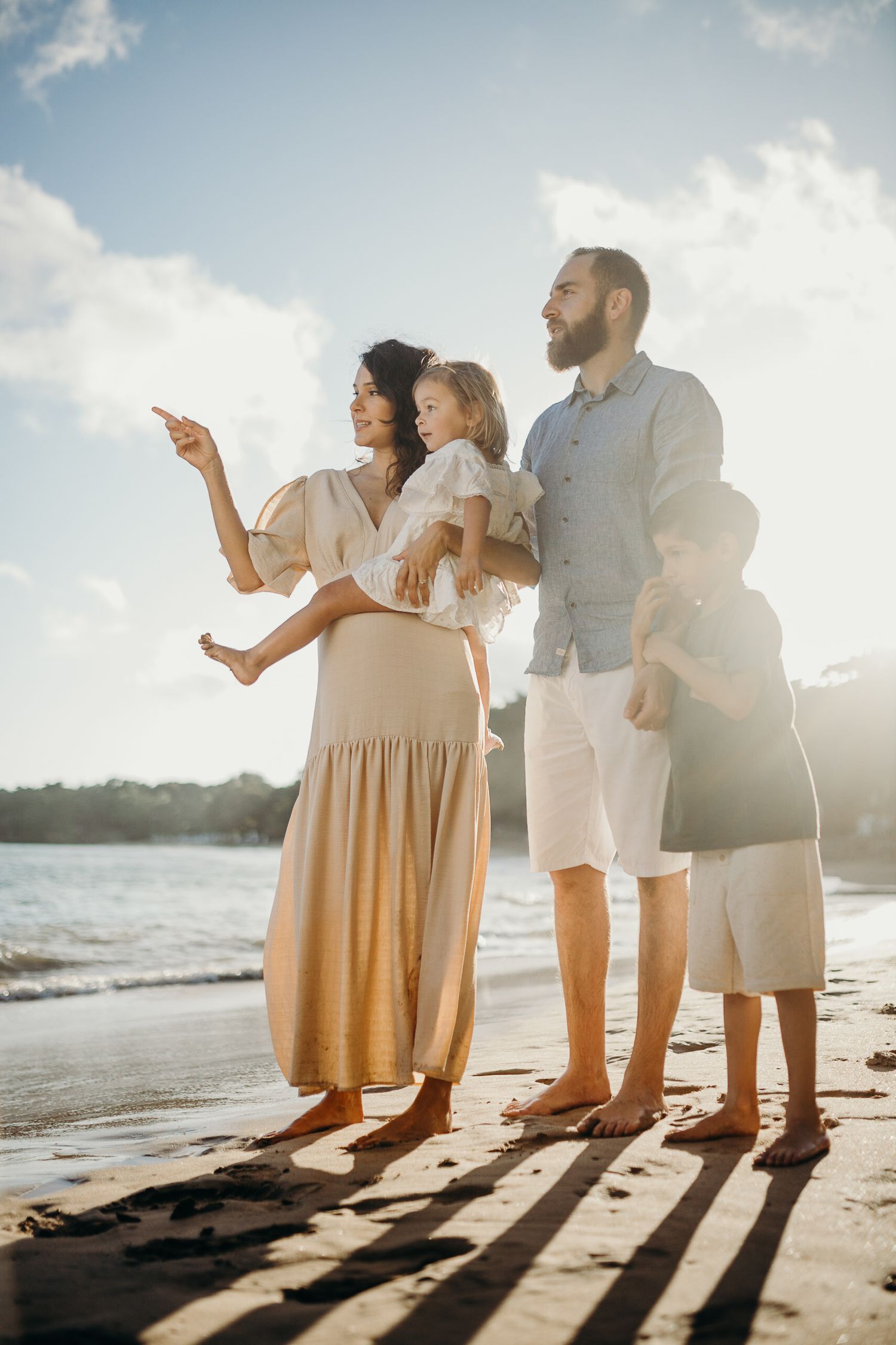 A family stands together on beach while pointing at something in the distance.