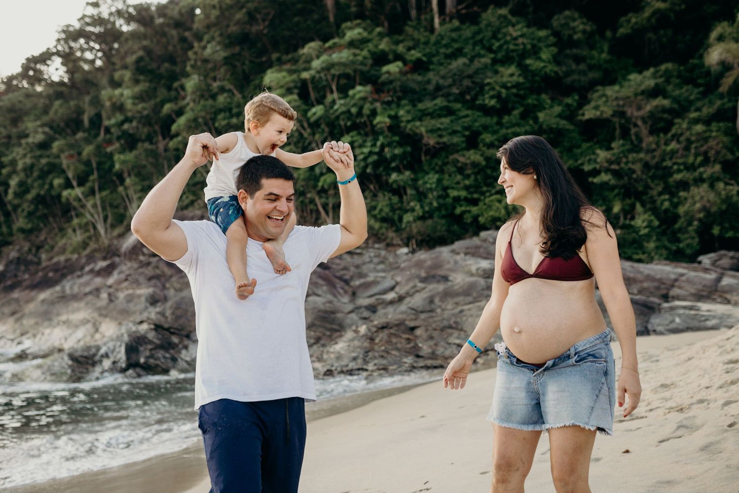 Happy family enjoying time together on a tropical beach with rock formations and forest backdrop.
