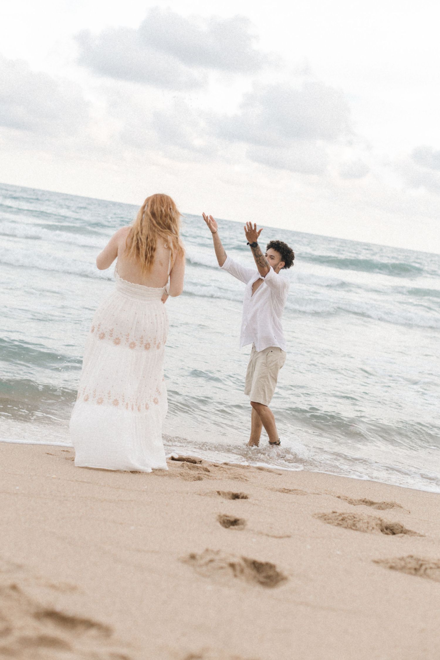 Playful couple dances and runs on the beach with waves crashing in the background.