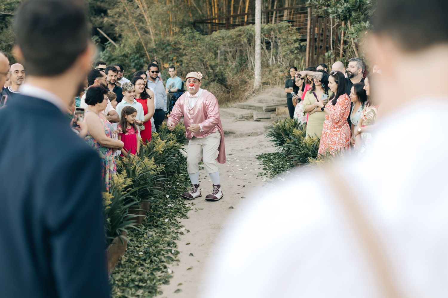 Wedding guest in pink outfit walks down outdoor path surrounded by attendees.