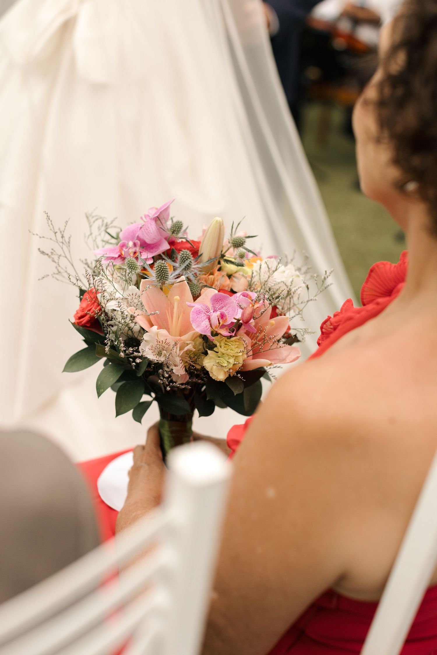 Pink and peach bridal bouquet with mixed flowers against white wedding dress.