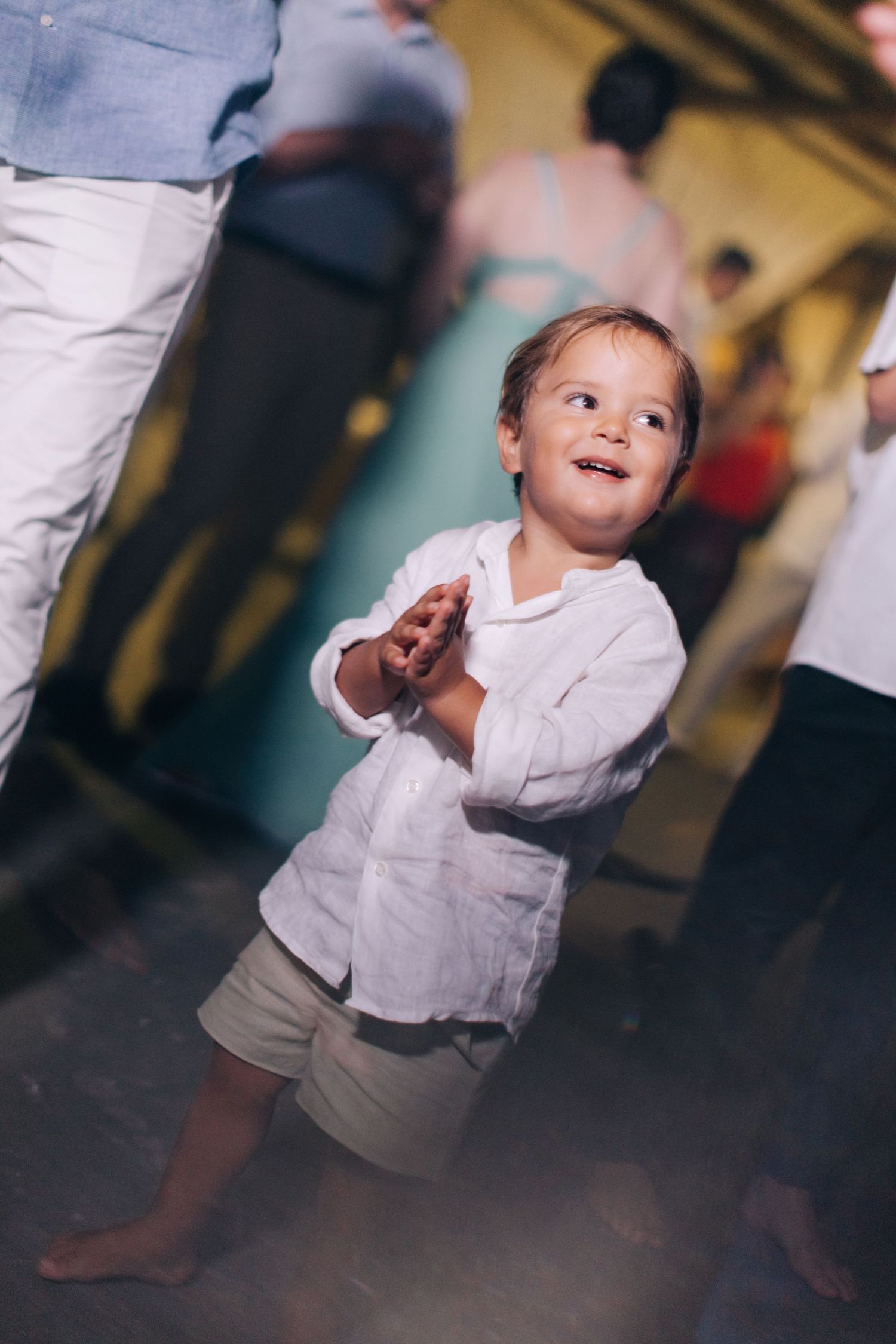 Young child in white shirt and khaki shorts dances barefoot at a celebration event.