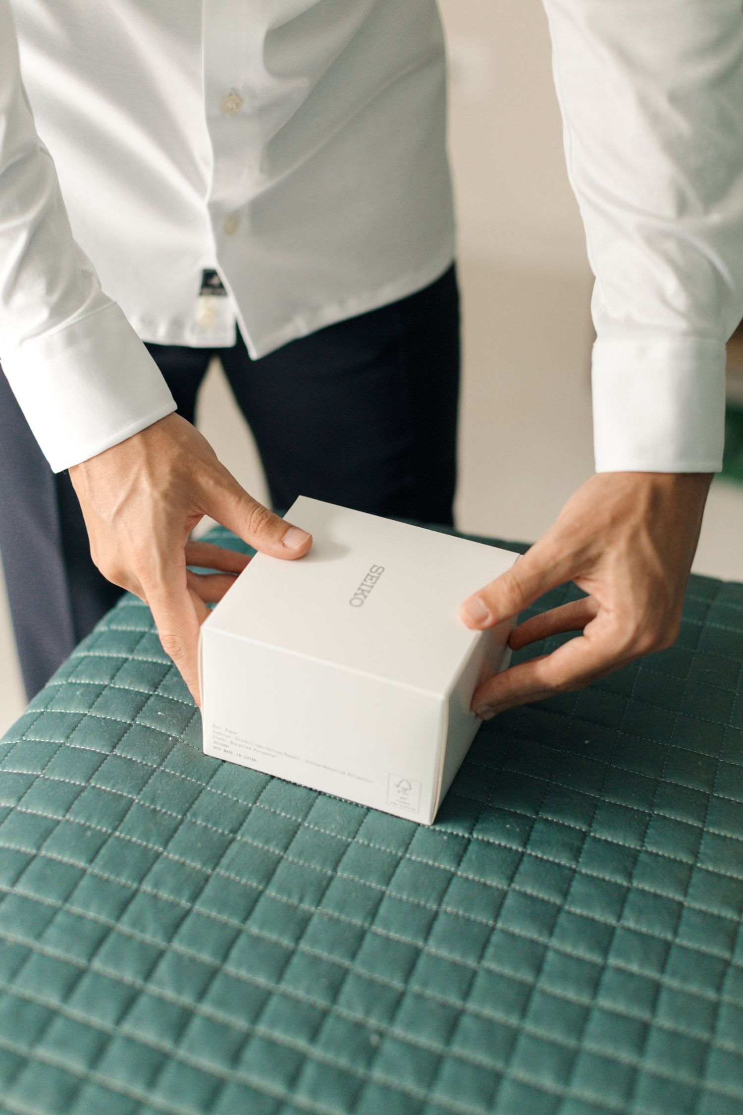 Hands carefully handle a white box on a teal quilted surface.