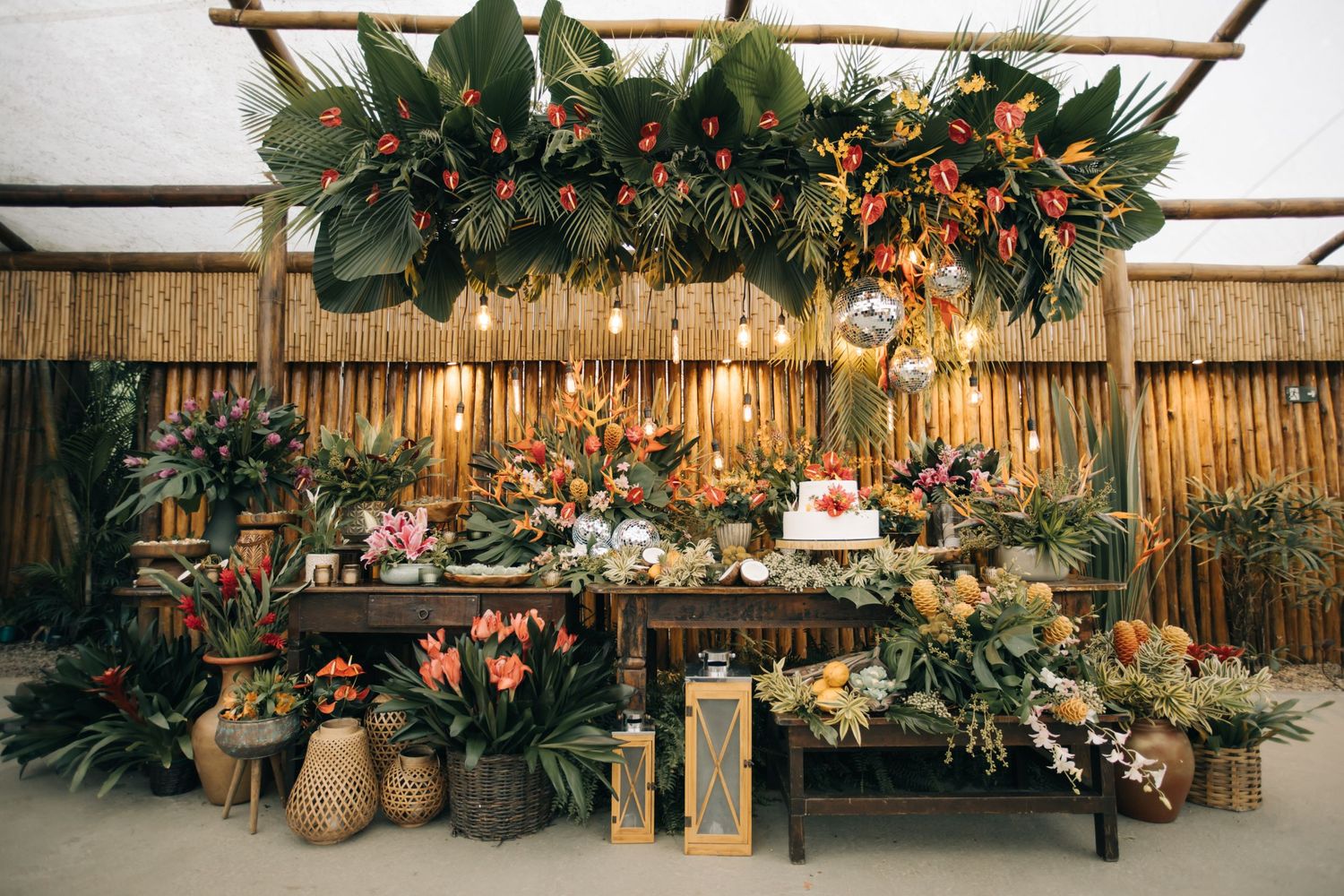Tropical wedding decor with greenery, lanterns and woven baskets against bamboo backdrop.