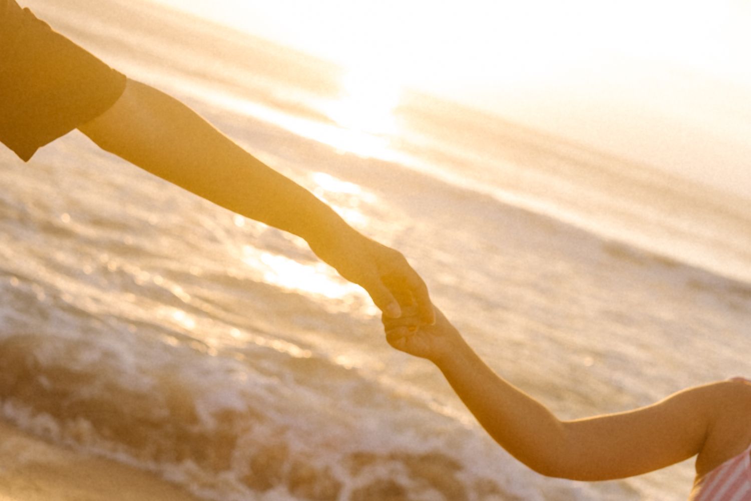 Duas pessoas de mãos dadas silhuetas contra um pôr do sol dourado sobre as ondas do mar.