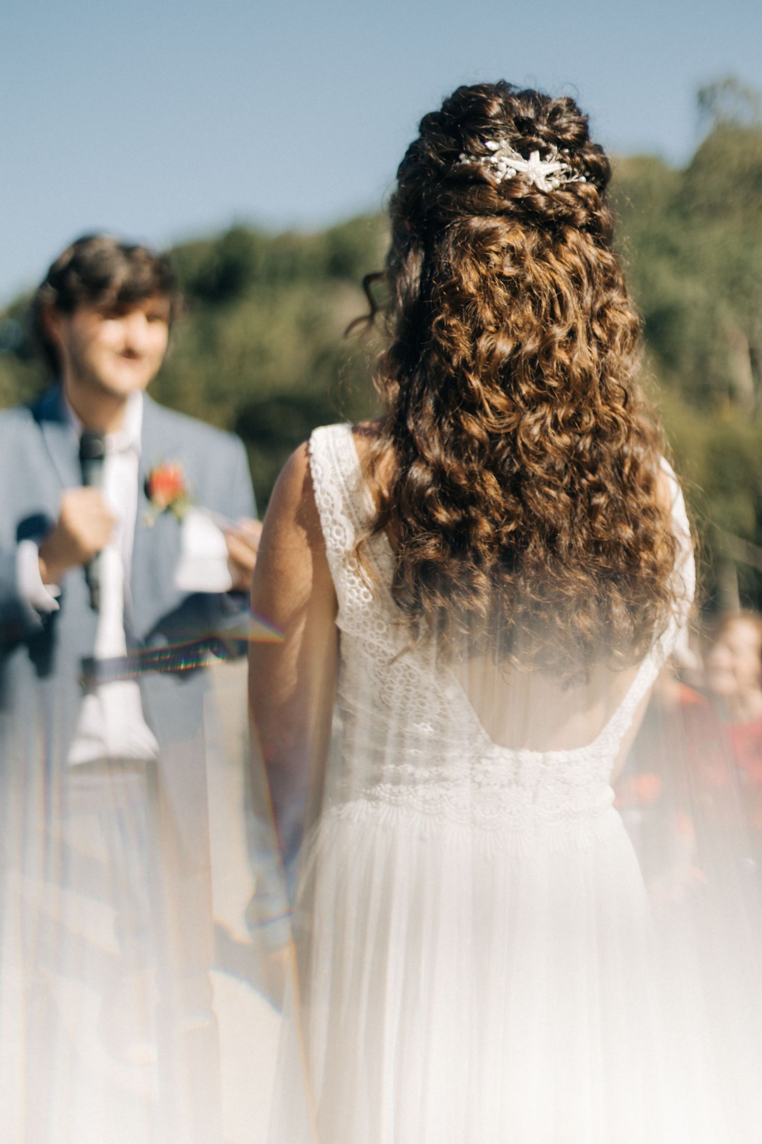 Back view of bride with curly hair during outdoor ceremony.