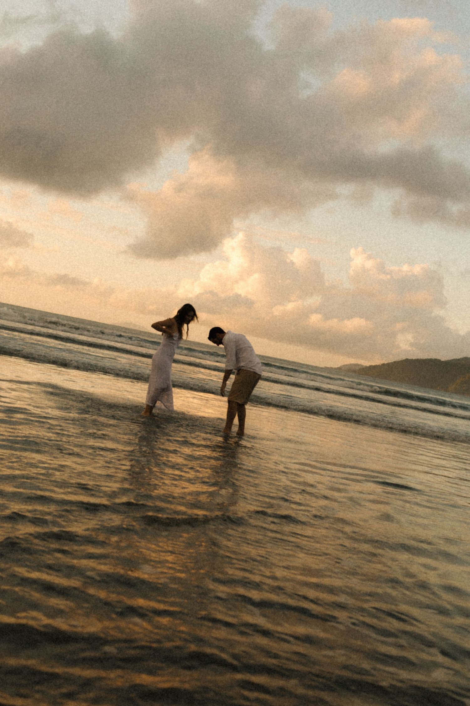 People splashing and playing in ocean waves during golden hour with dramatic clouds overhead.