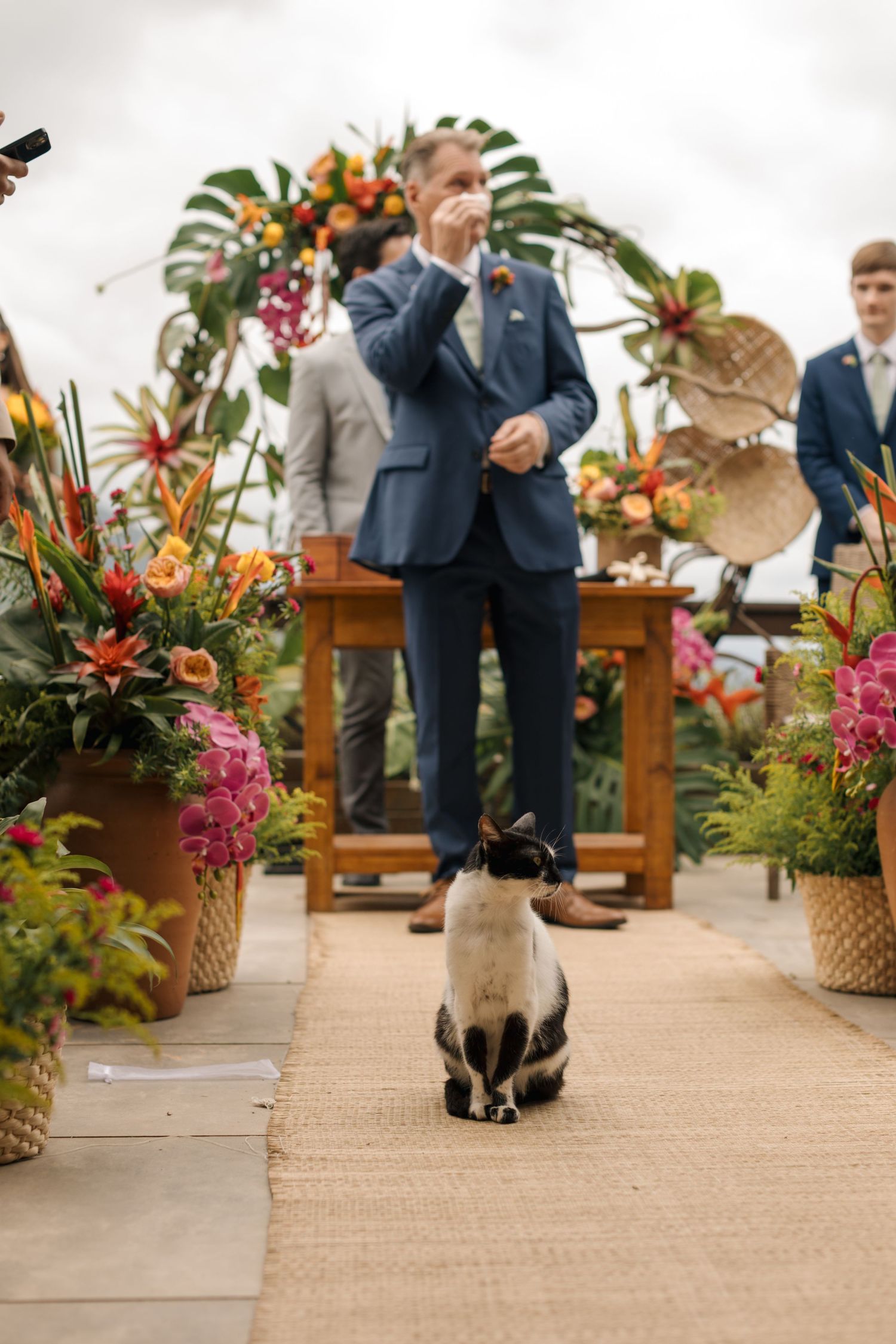 Tropical floral arrangements with bright orange and pink blooms line a burlap-covered aisle.