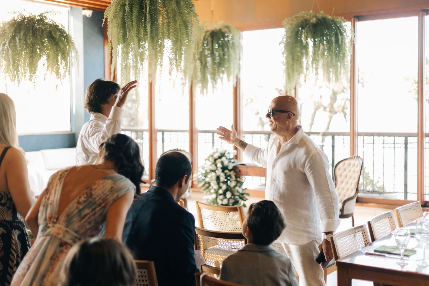 Wedding celebration in a room decorated with hanging plants and large windows.