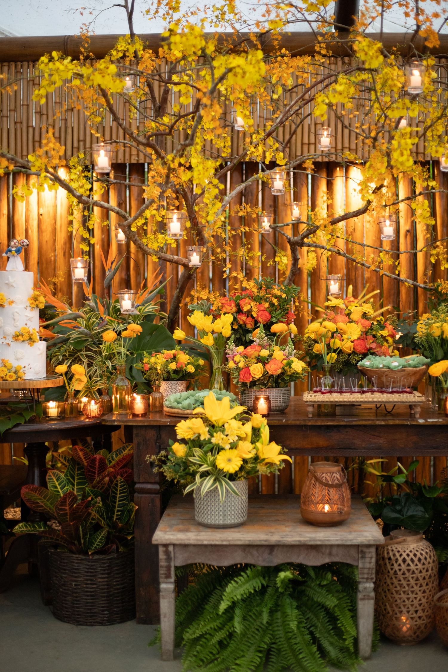 Wedding reception decor featuring yellow orchids, hanging lights, and wooden elements against a bamboo wall.
