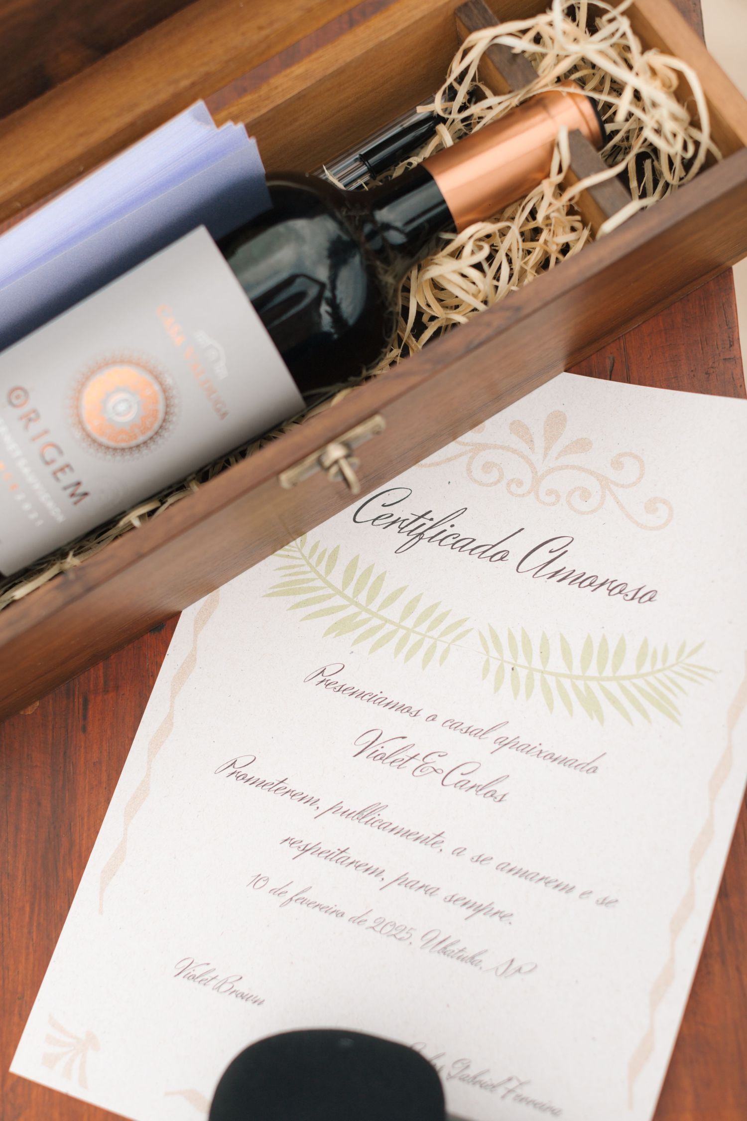Wedding invitation and wine bottle displayed in elegant wooden box with decorative straw.