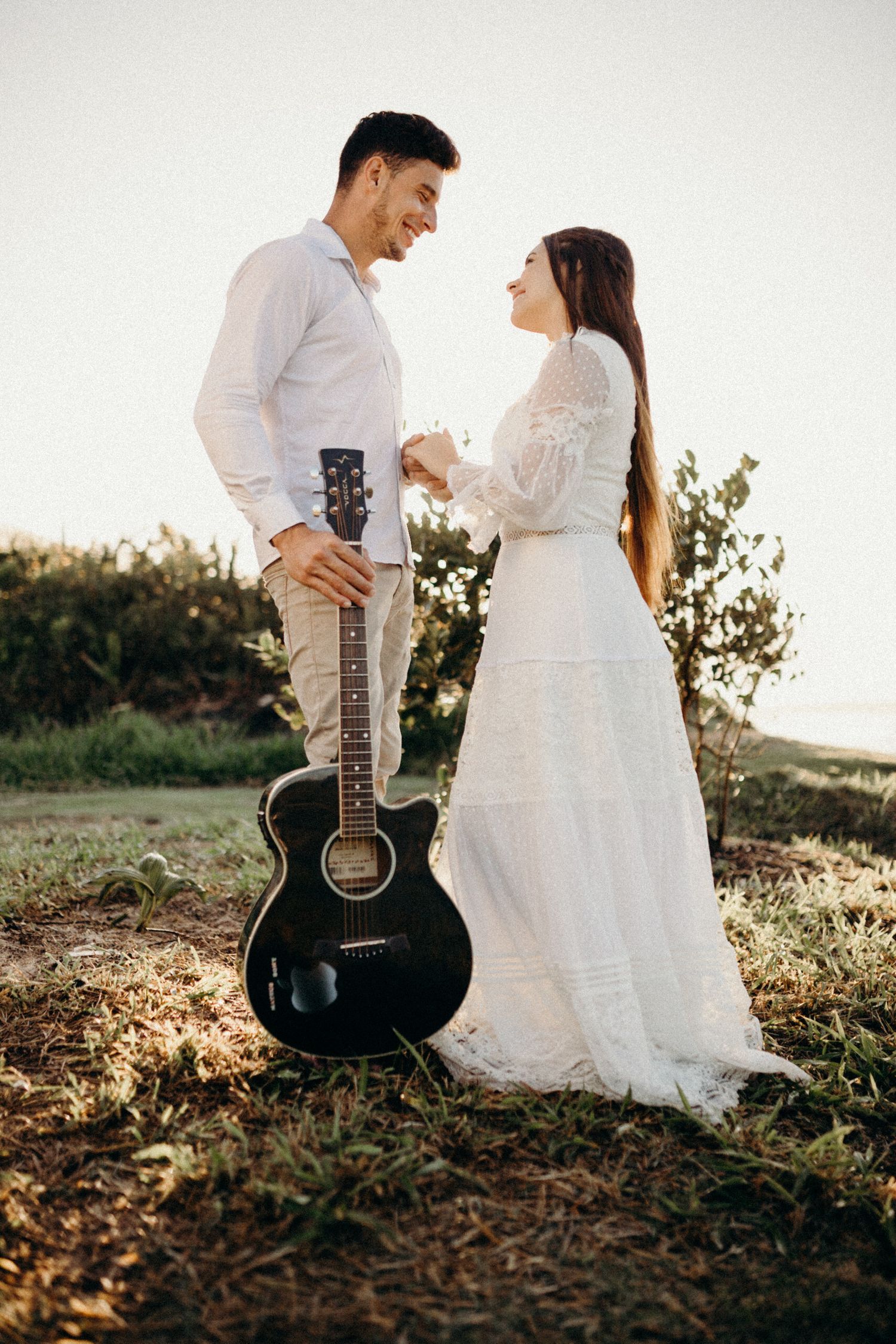 Couple shares intimate moment outdoors with black acoustic guitar during sunset photoshoot.