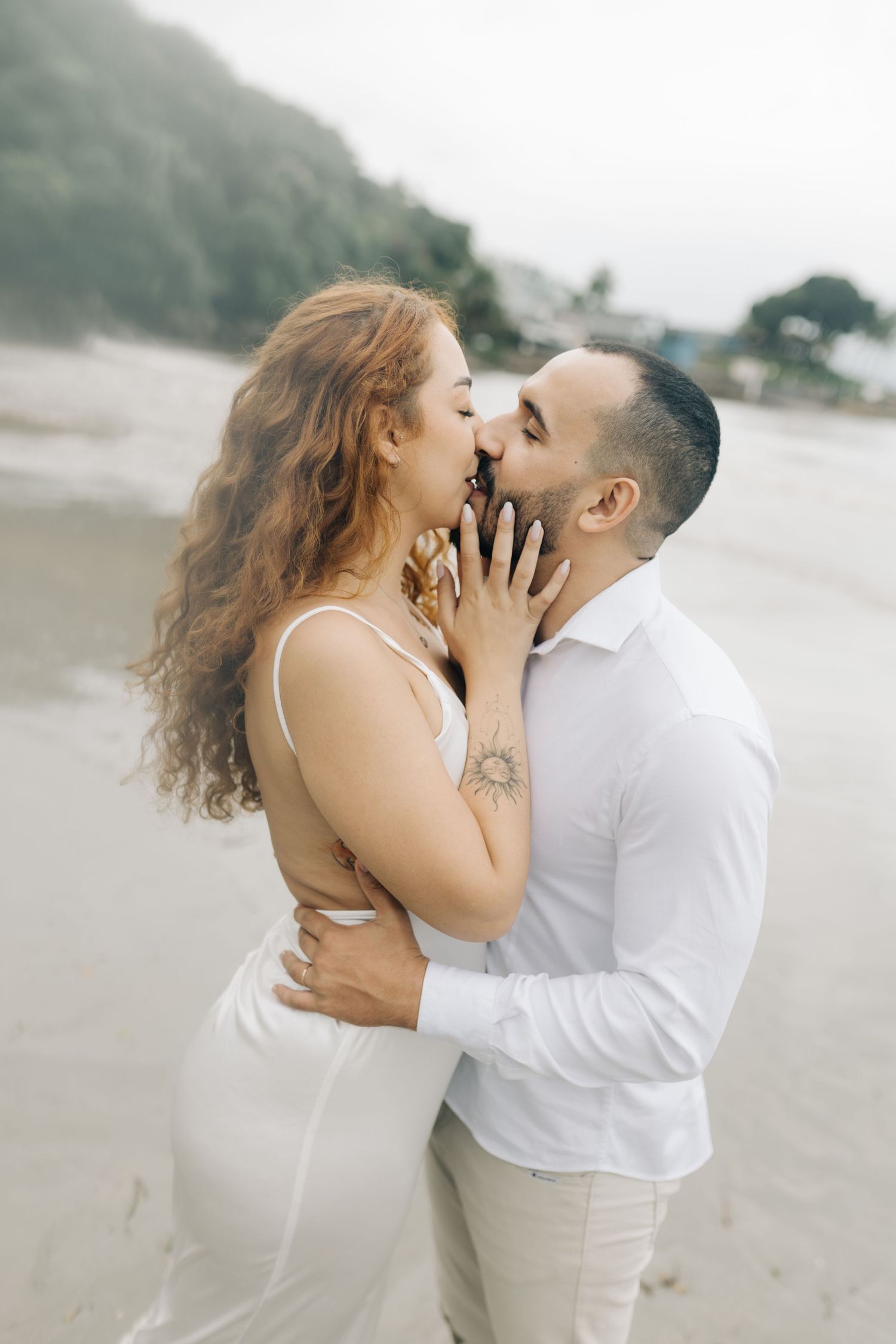 Romantic seaside photoshoot featuring an intimate moment between a couple on a cloudy beach.