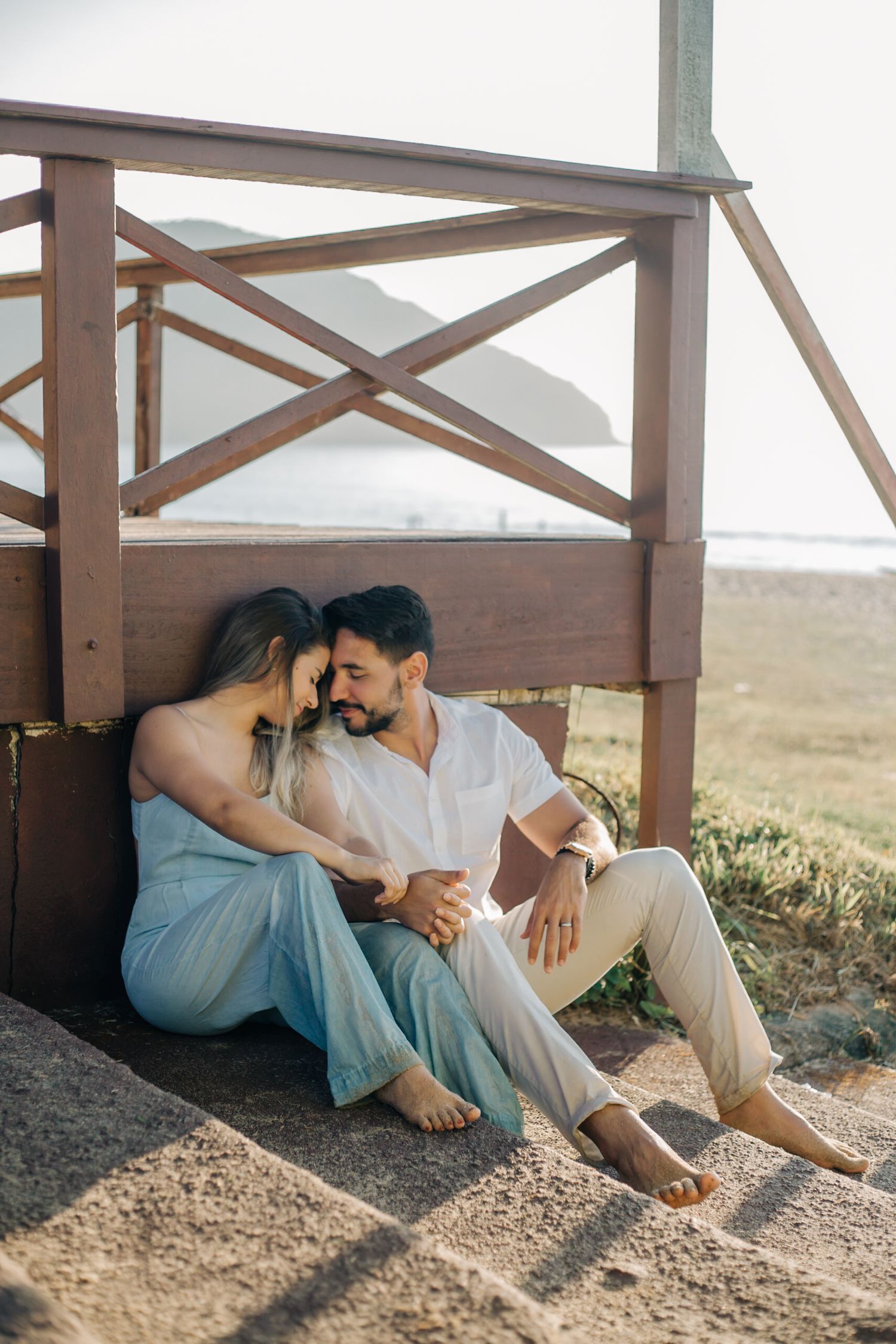 Romantic couple sharing an intimate moment on a rustic wooden porch overlooking a scenic landscape at sunset.