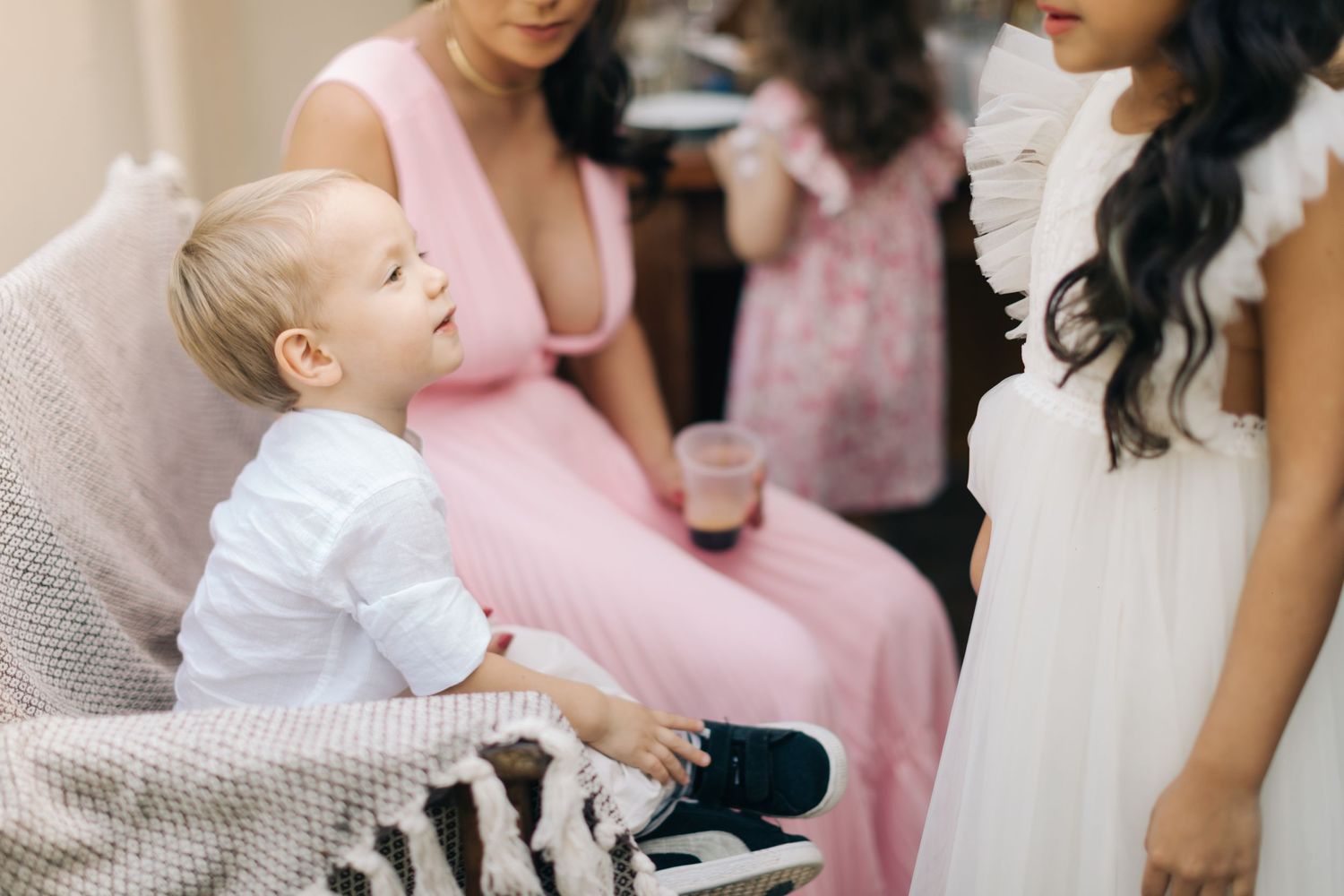 Baby in white outfit sitting with adults in formal dress during special occasion.