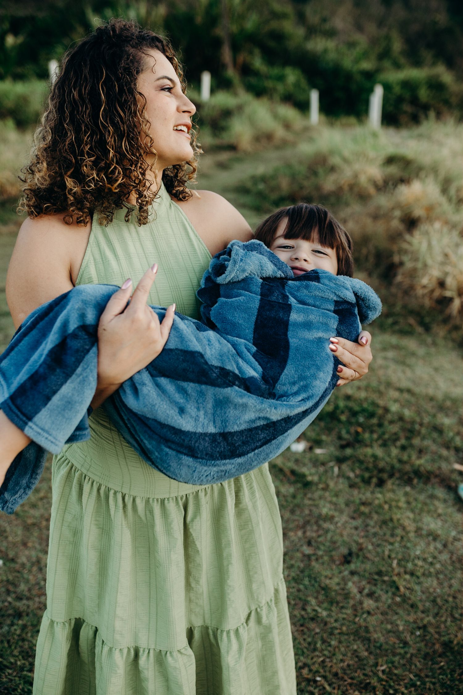 A woman in a green dress holds a child wrapped in a blue blanket outdoors.