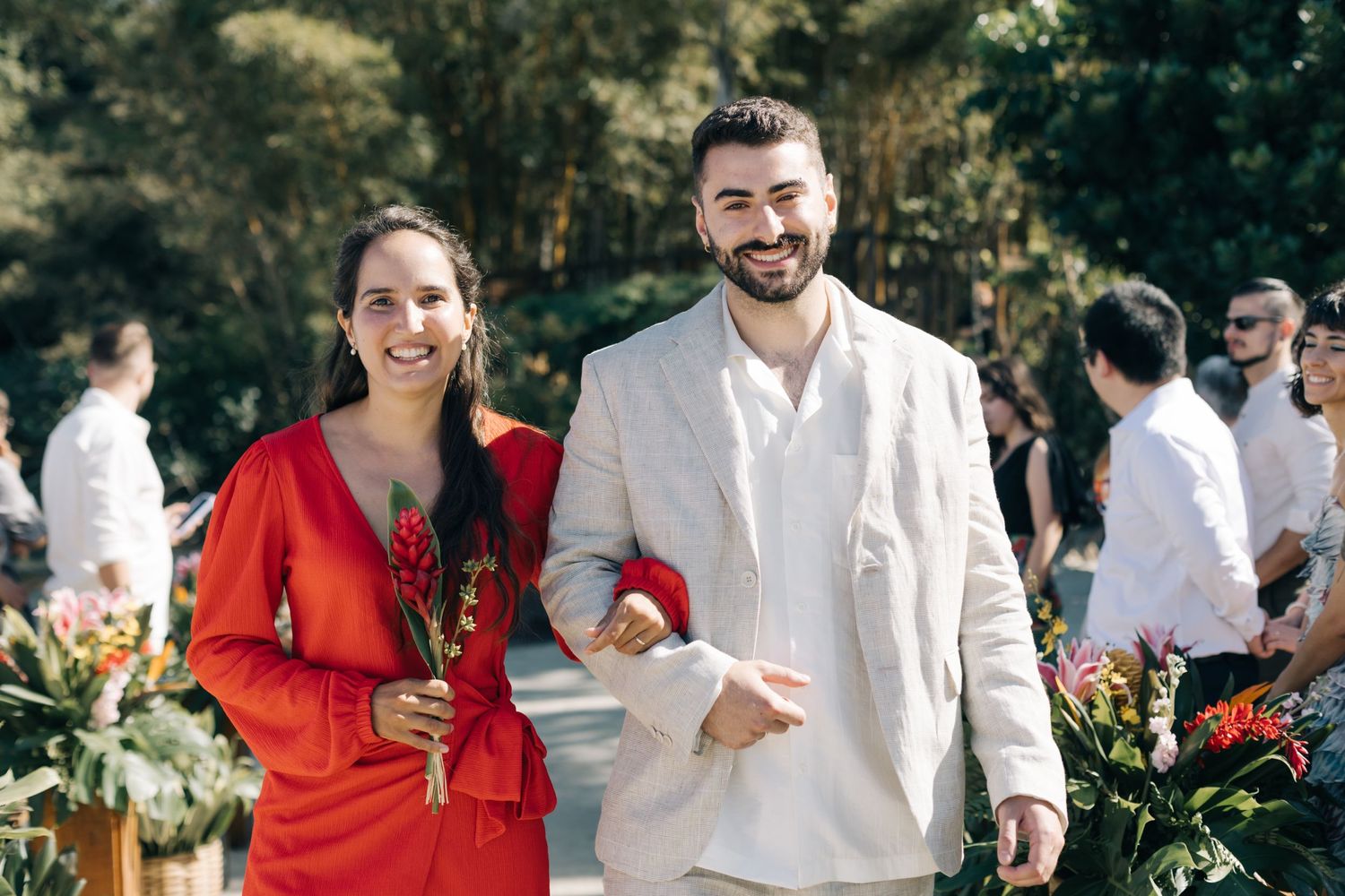 Outdoor wedding gathering with guests in bright red and white attire.