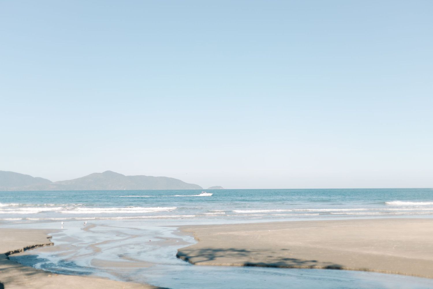 Serene coastal landscape with mountains and beach in soft pastel tones.