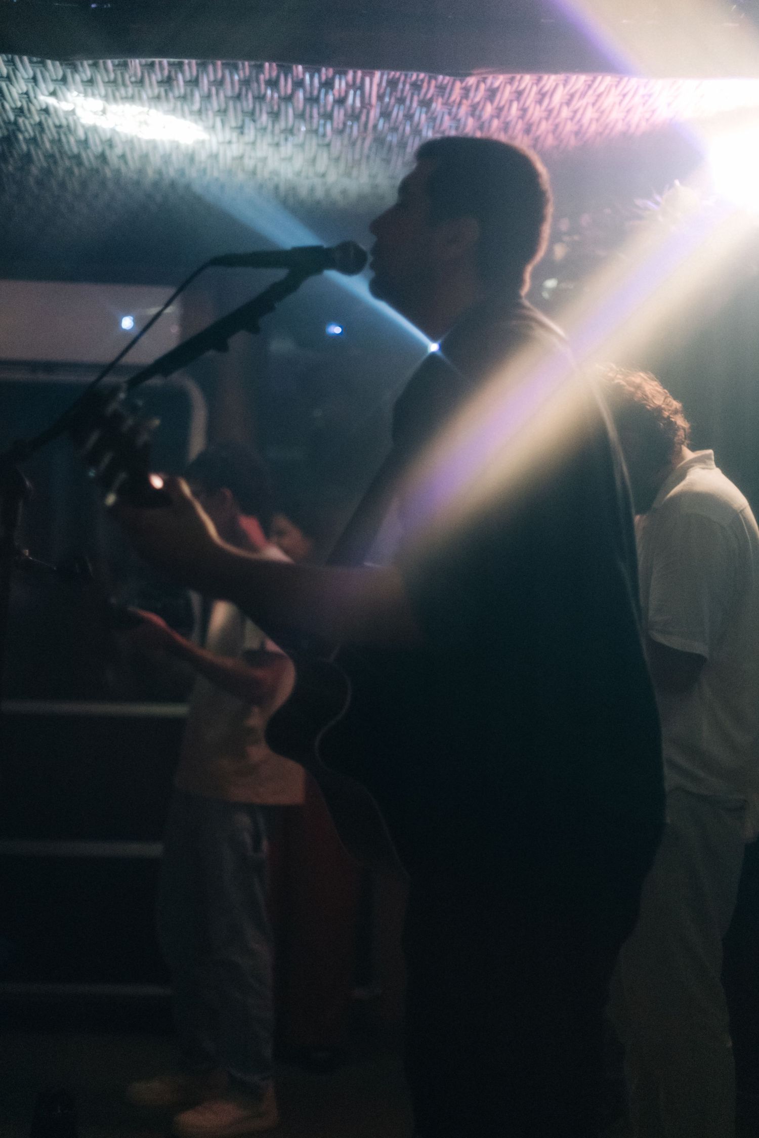 Silhouette of a performer singing at a dimly lit venue with stage lighting effects.