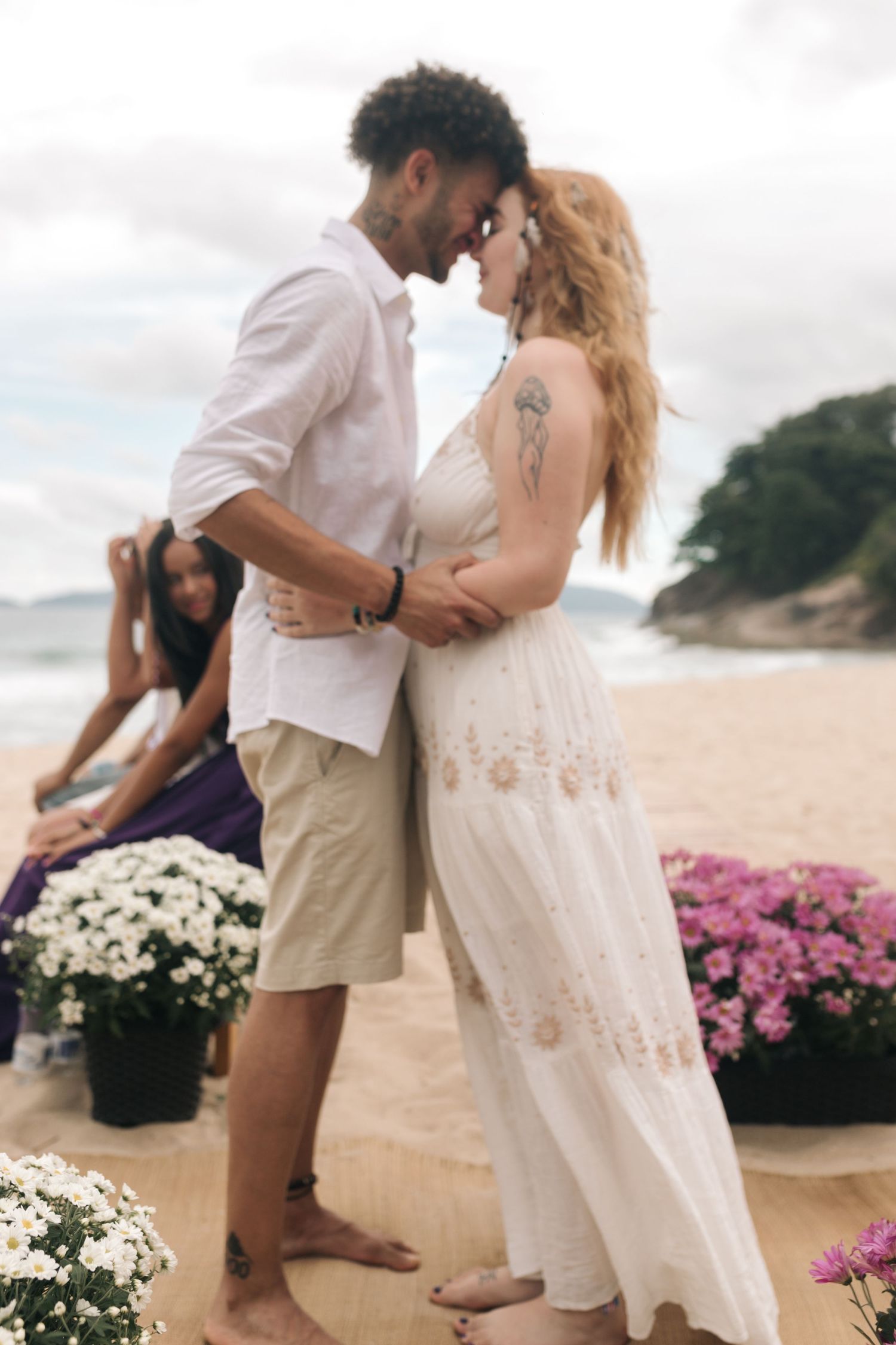 A tender moment between newlyweds on a beach with floral decorations and ocean backdrop.
