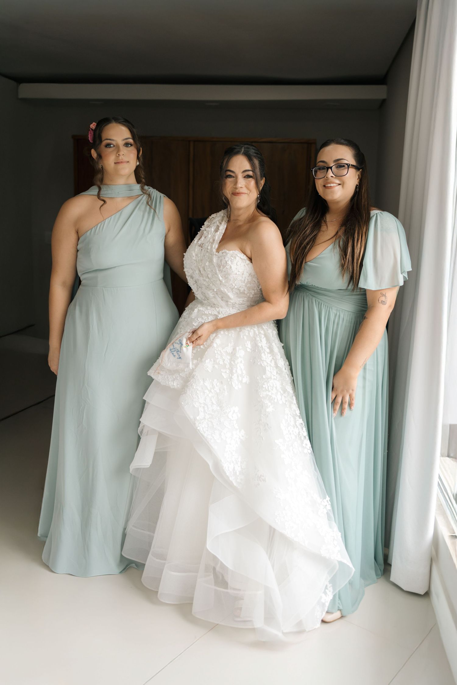 Wedding party members in mint green dresses pose together indoors.