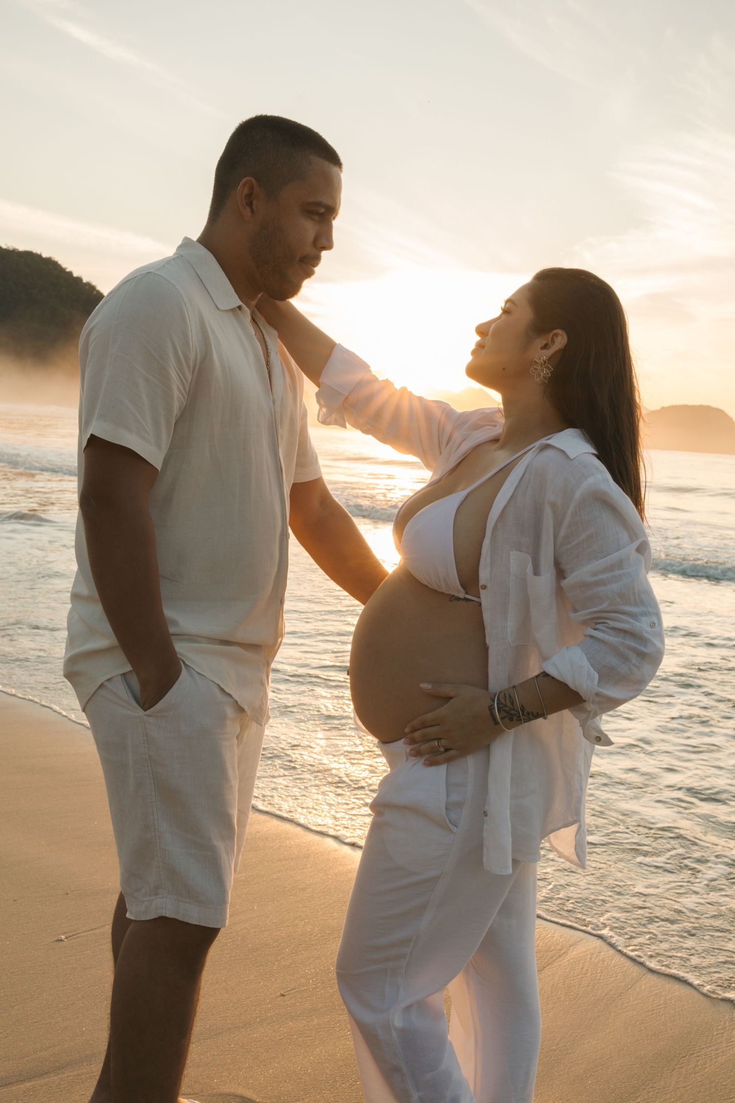 Sunset beach maternity photo showing couple in white sharing tender moment.