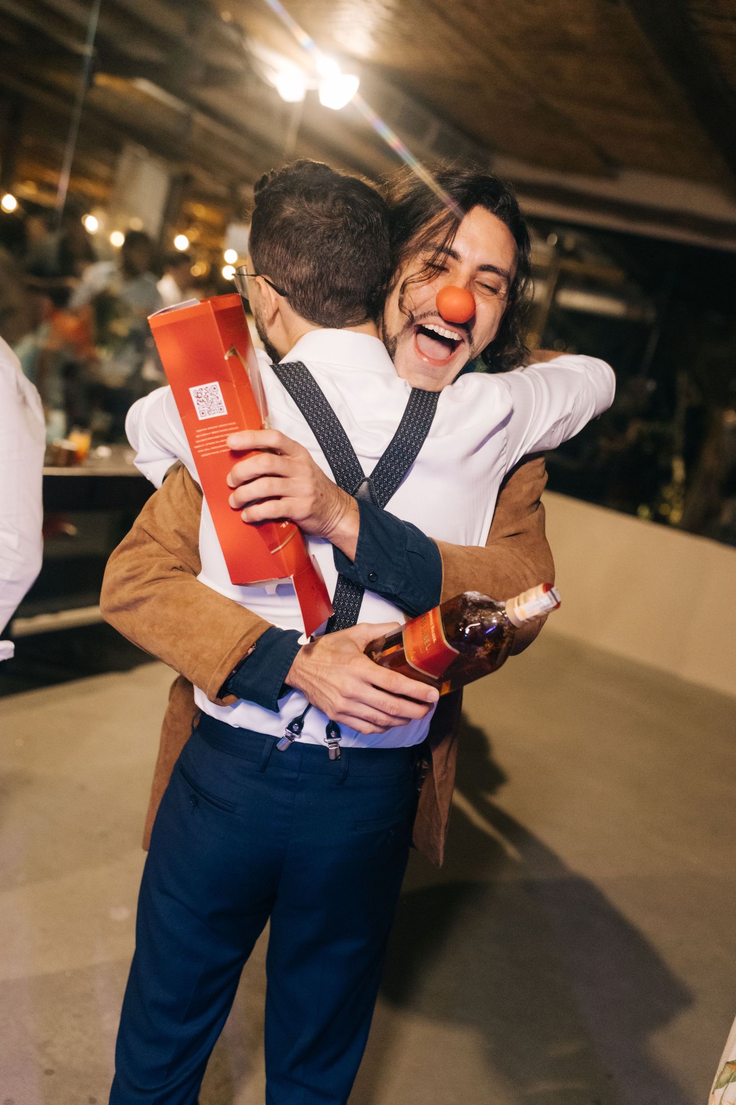 Two guests embracing and celebrating with drinks at wedding reception.