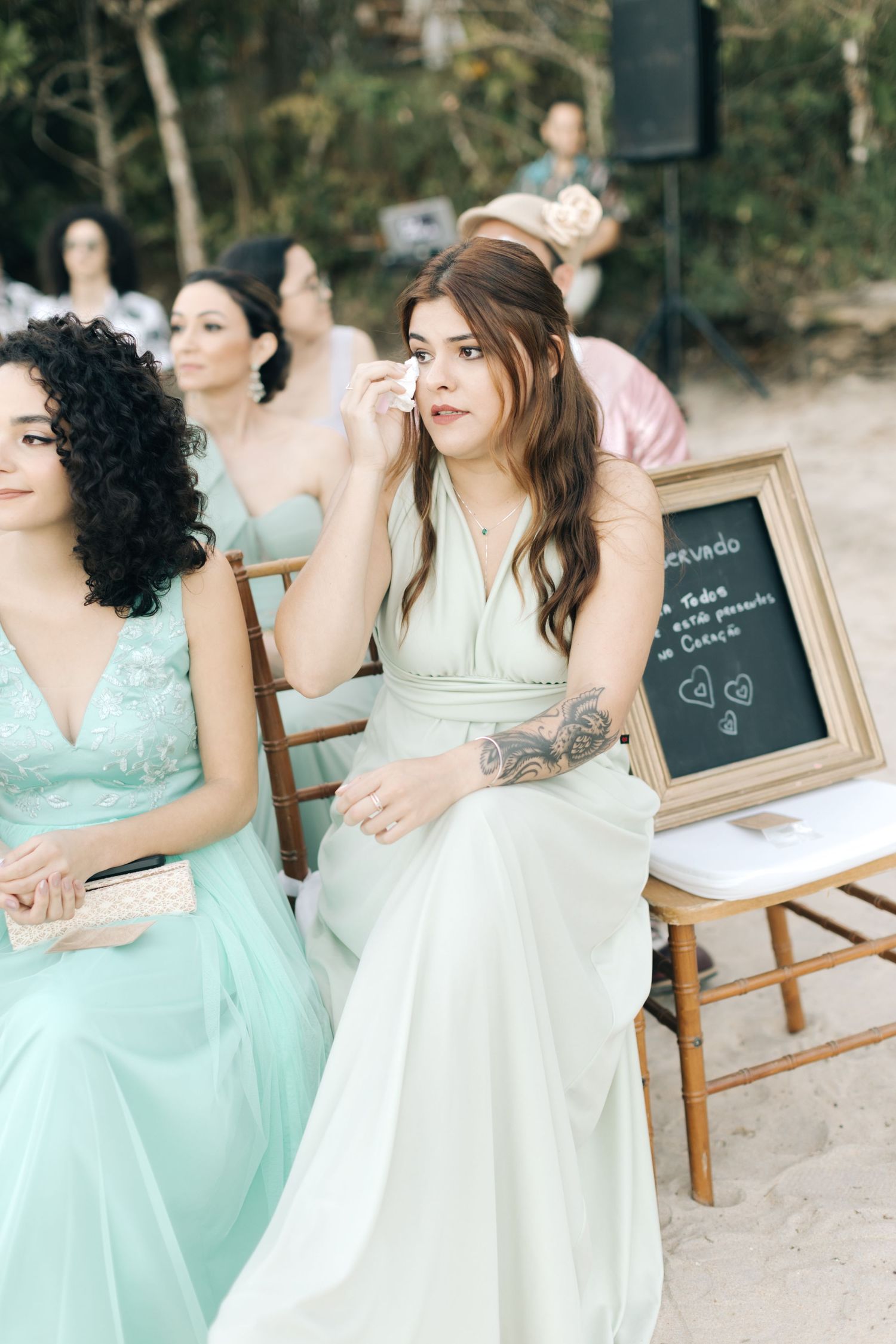 Wedding guests seated at outdoor ceremony with decorative chalkboard sign.