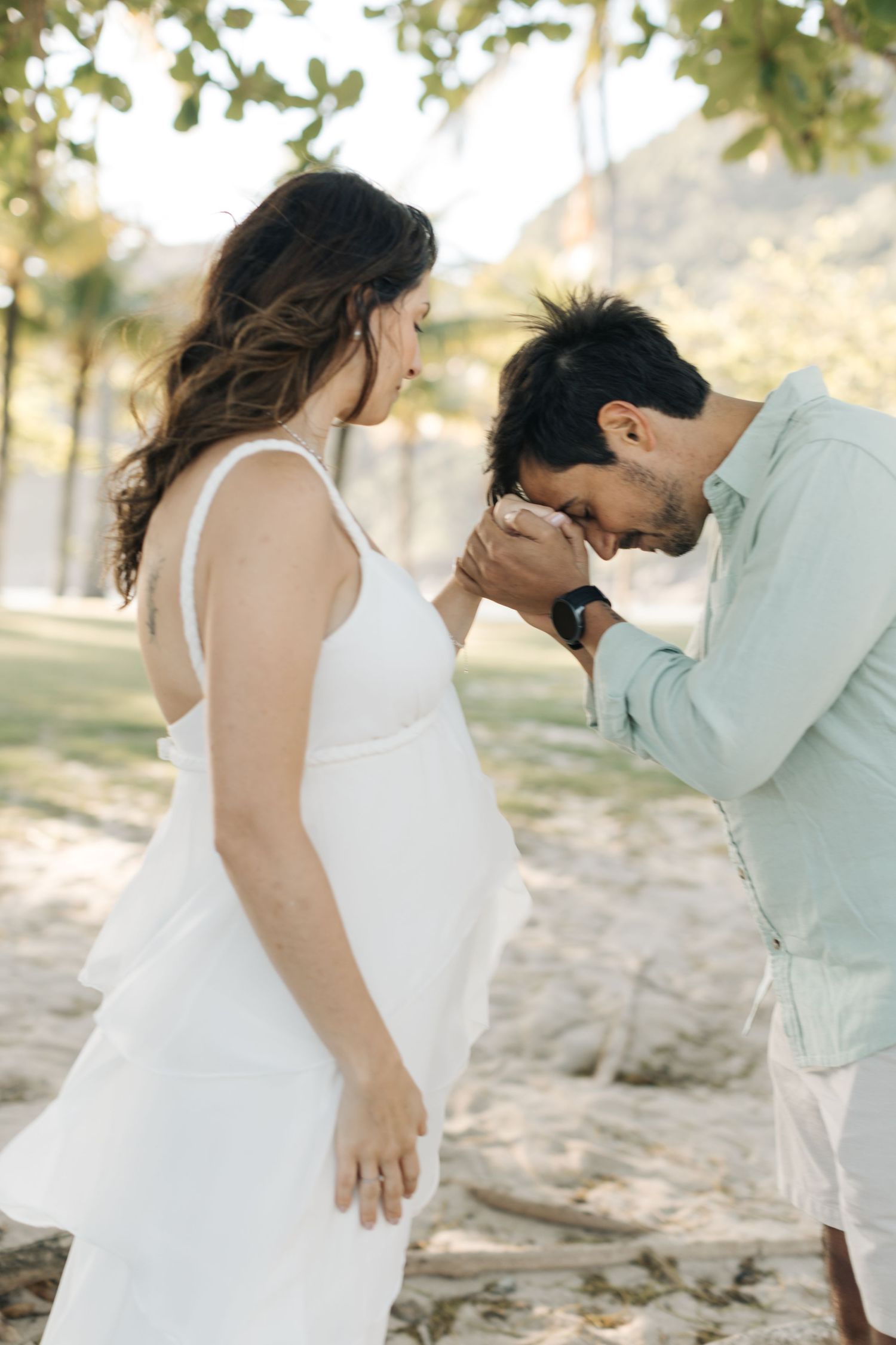 A romantic moment between a couple in wedding attire standing on rocks with sunlit trees in the background.