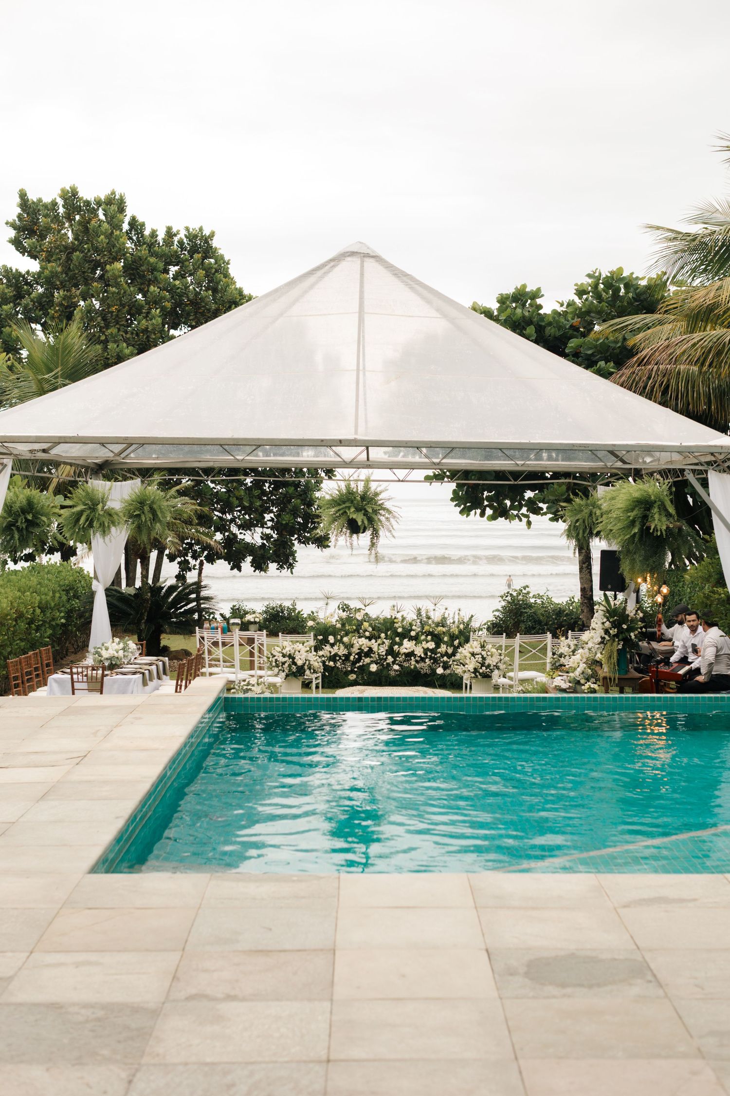 Elegant white tent pavilion overlooking swimming pool with tropical landscaping.