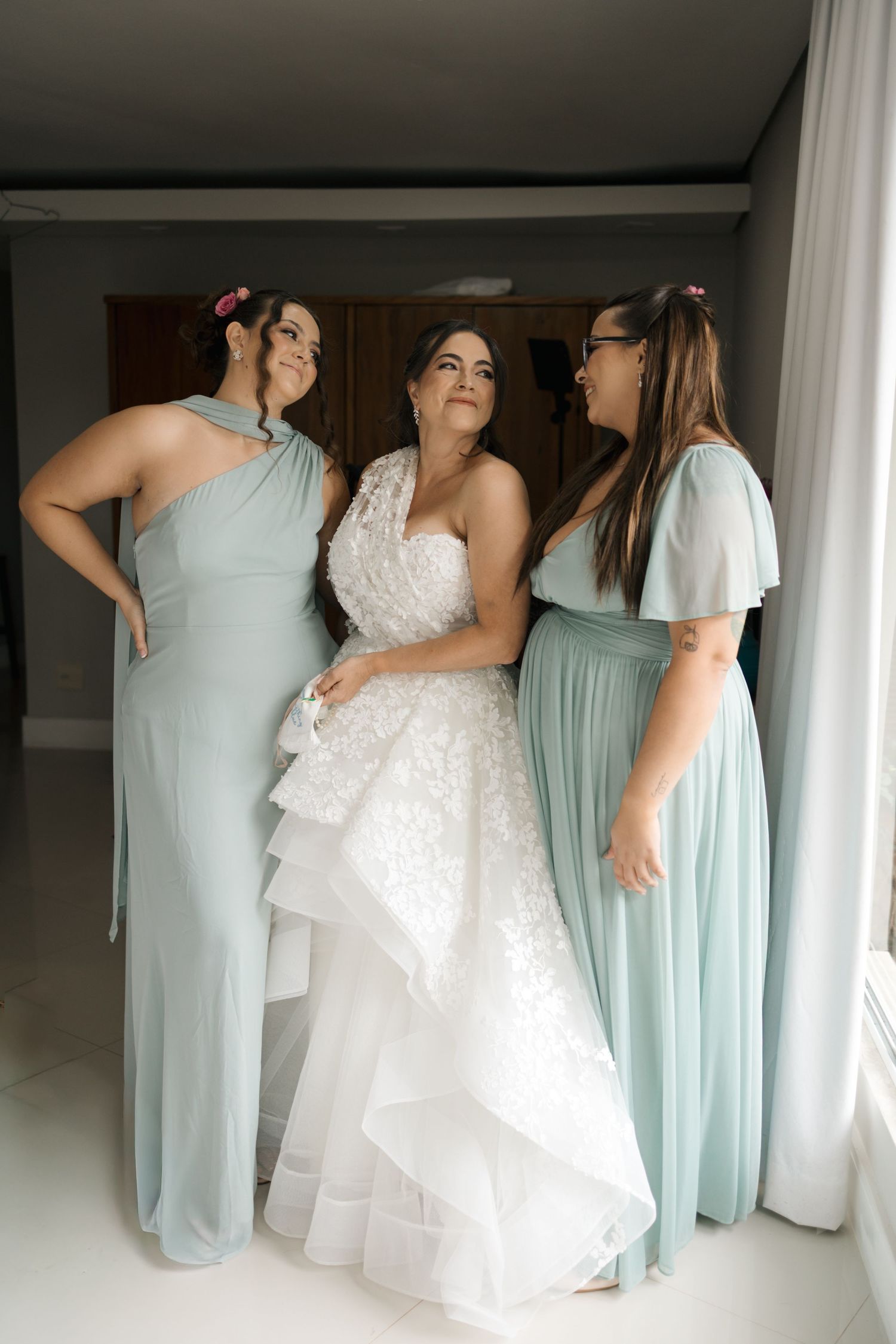 Bridesmaids in mint green dresses help adjust a white wedding gown in an indoor setting.