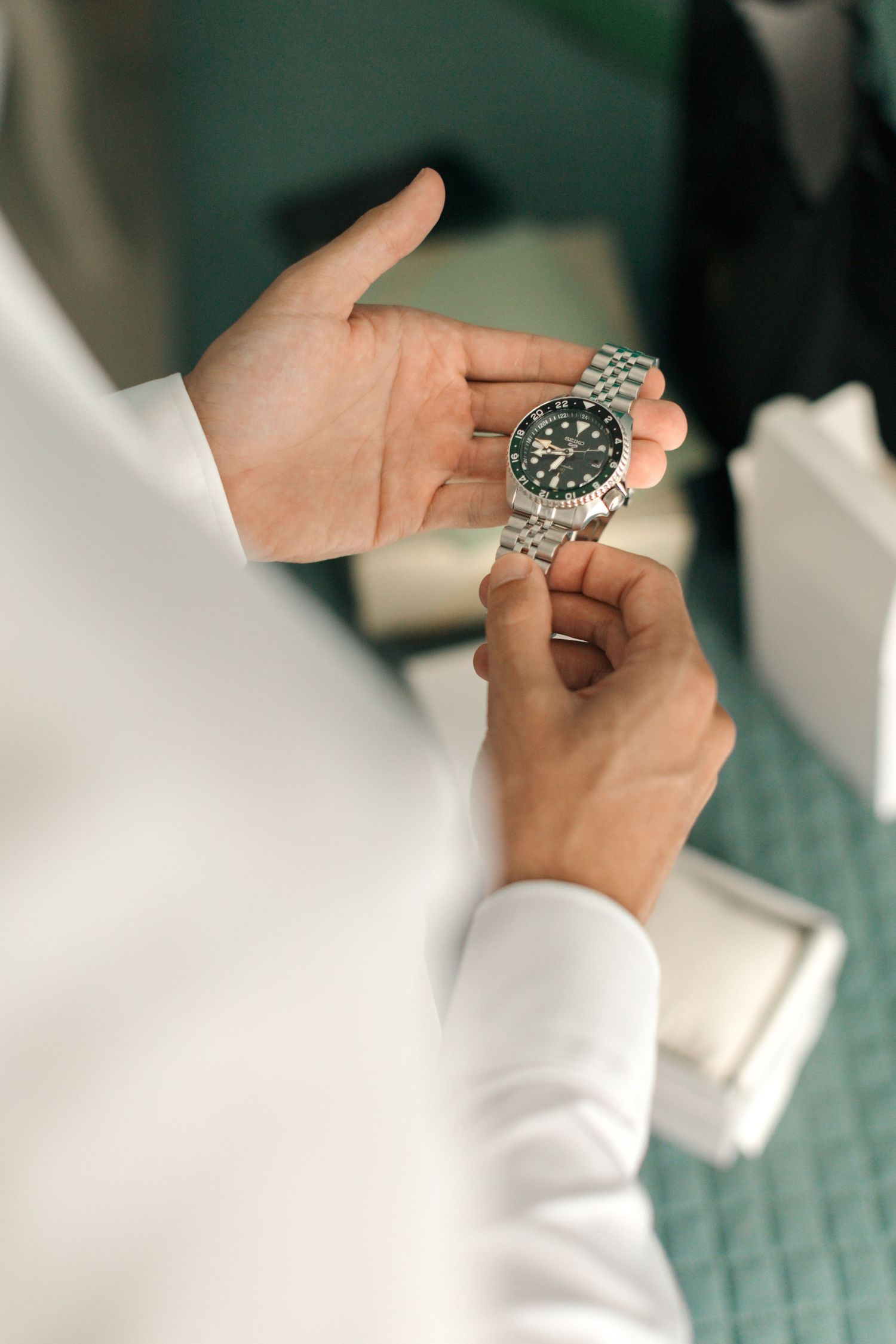 Close-up of hands holding a silver watch against a turquoise background.